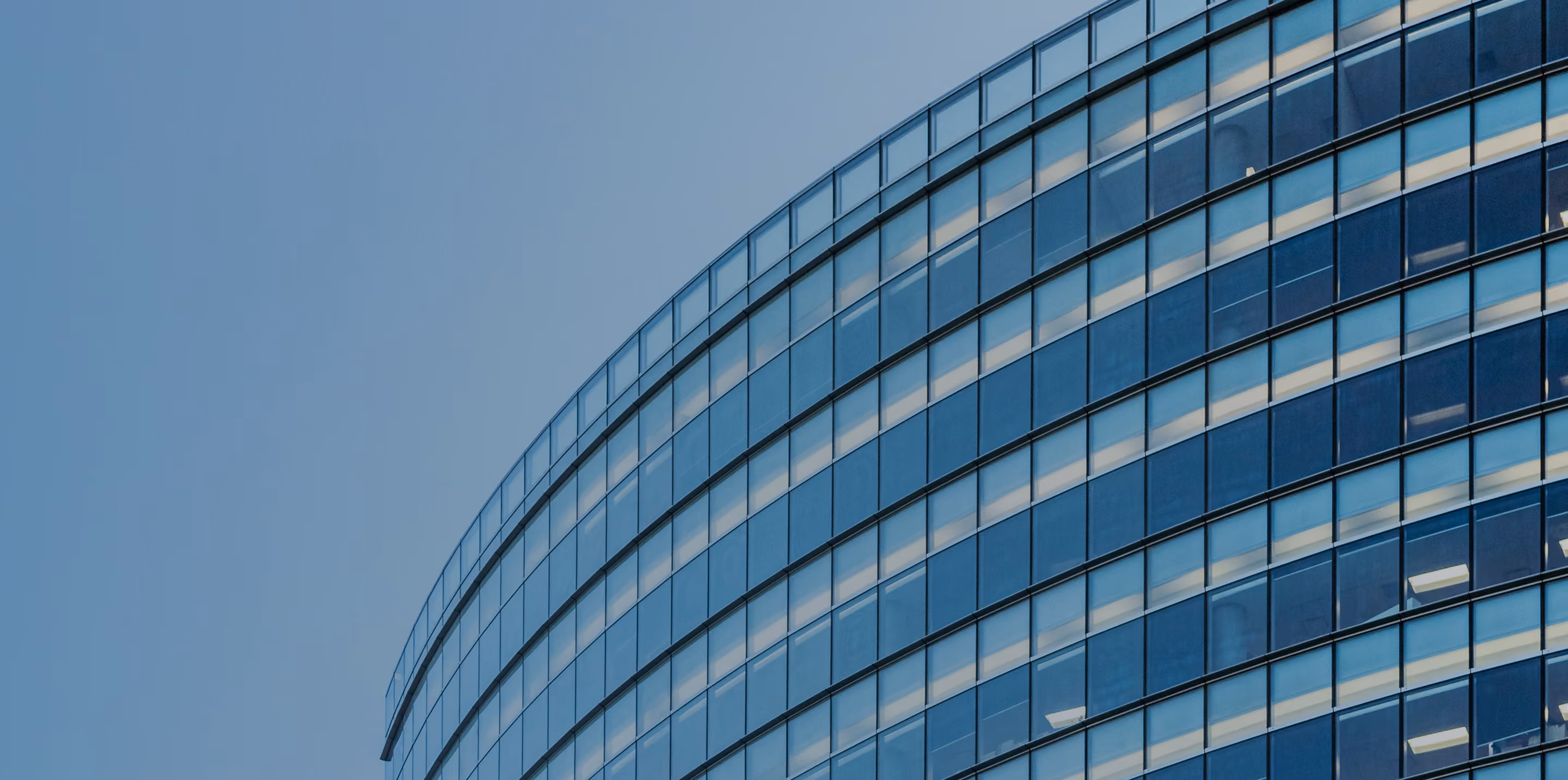 Curved modern office building with reflective glass windows under clear blue sky.