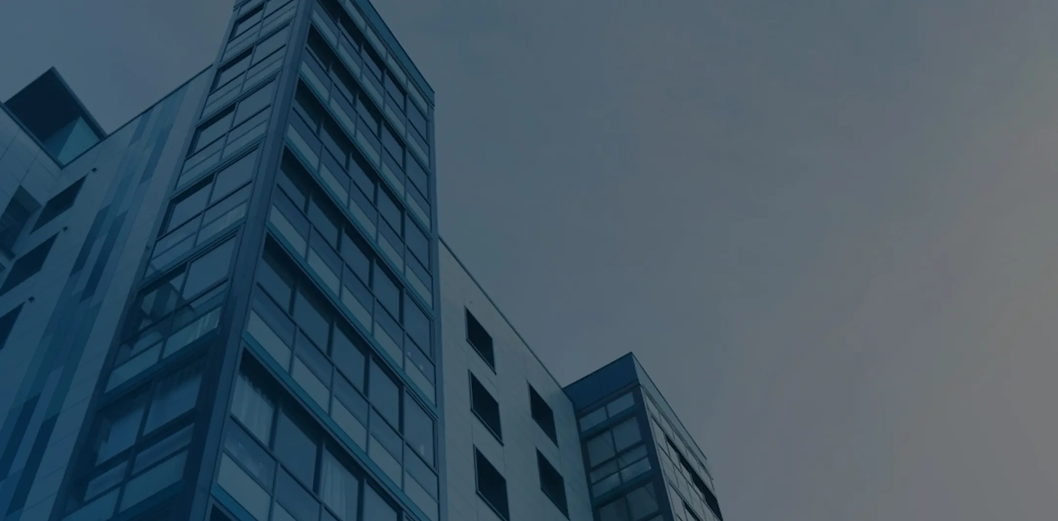 Low-angle view of a modern multi-story building with glass windows against a gray sky.