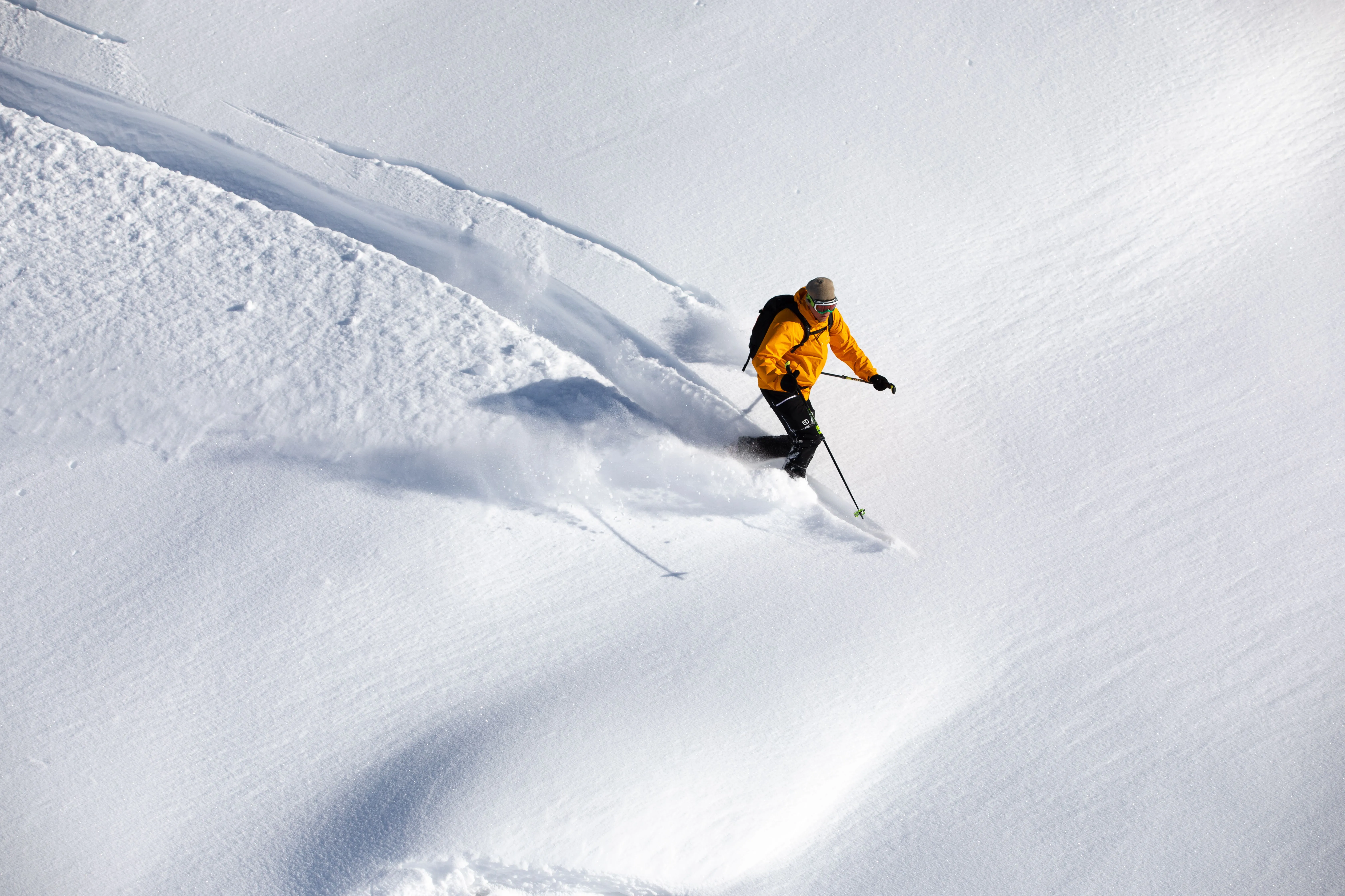 Skier in an orange jacket skiing down powder snow on a sunny day.