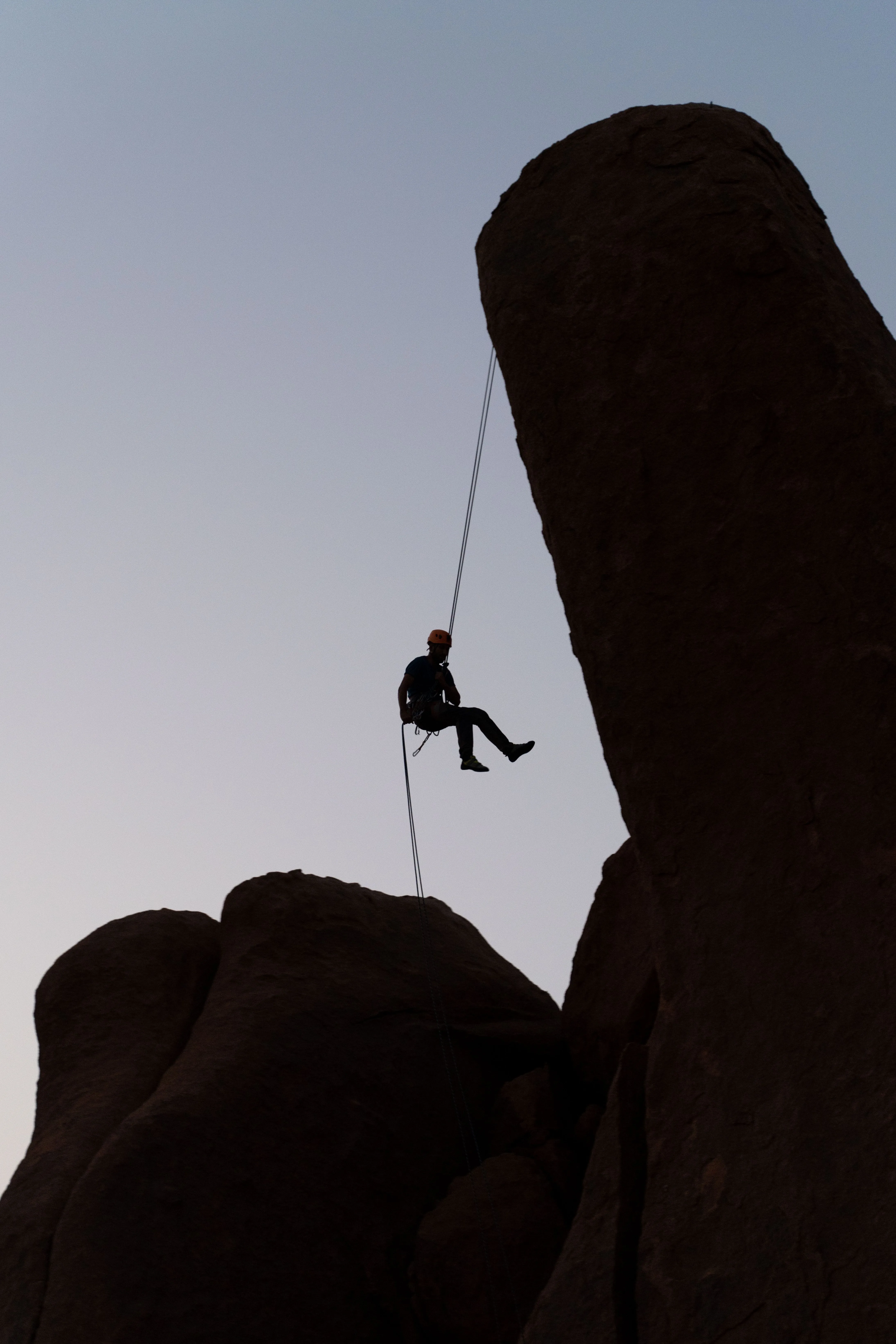 Silhouette of a person rappelling down large rock formations at dusk.