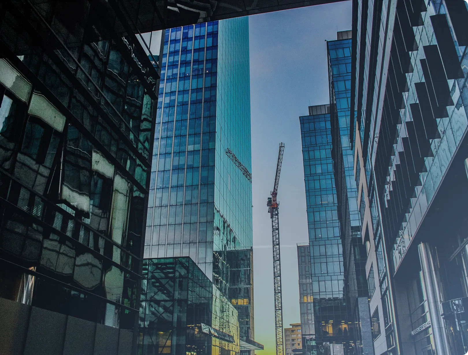 Construction crane among tall glass skyscrapers in an urban area during sunset.