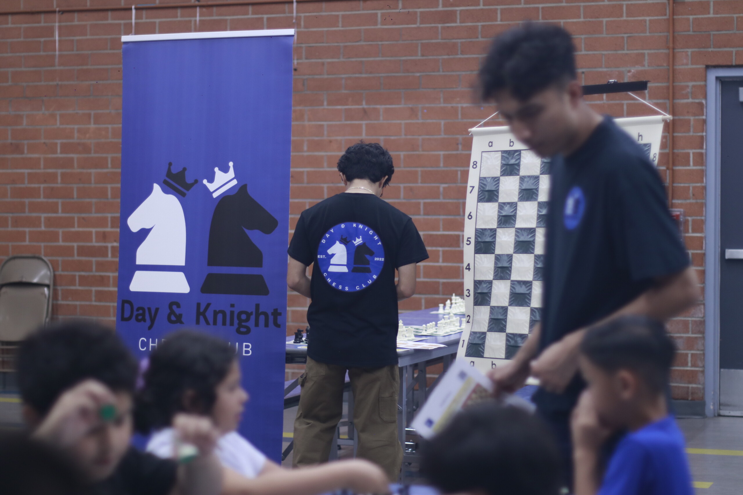 After-school chess club with kids playing chess, a chessboard, and a Day & Knight banner.