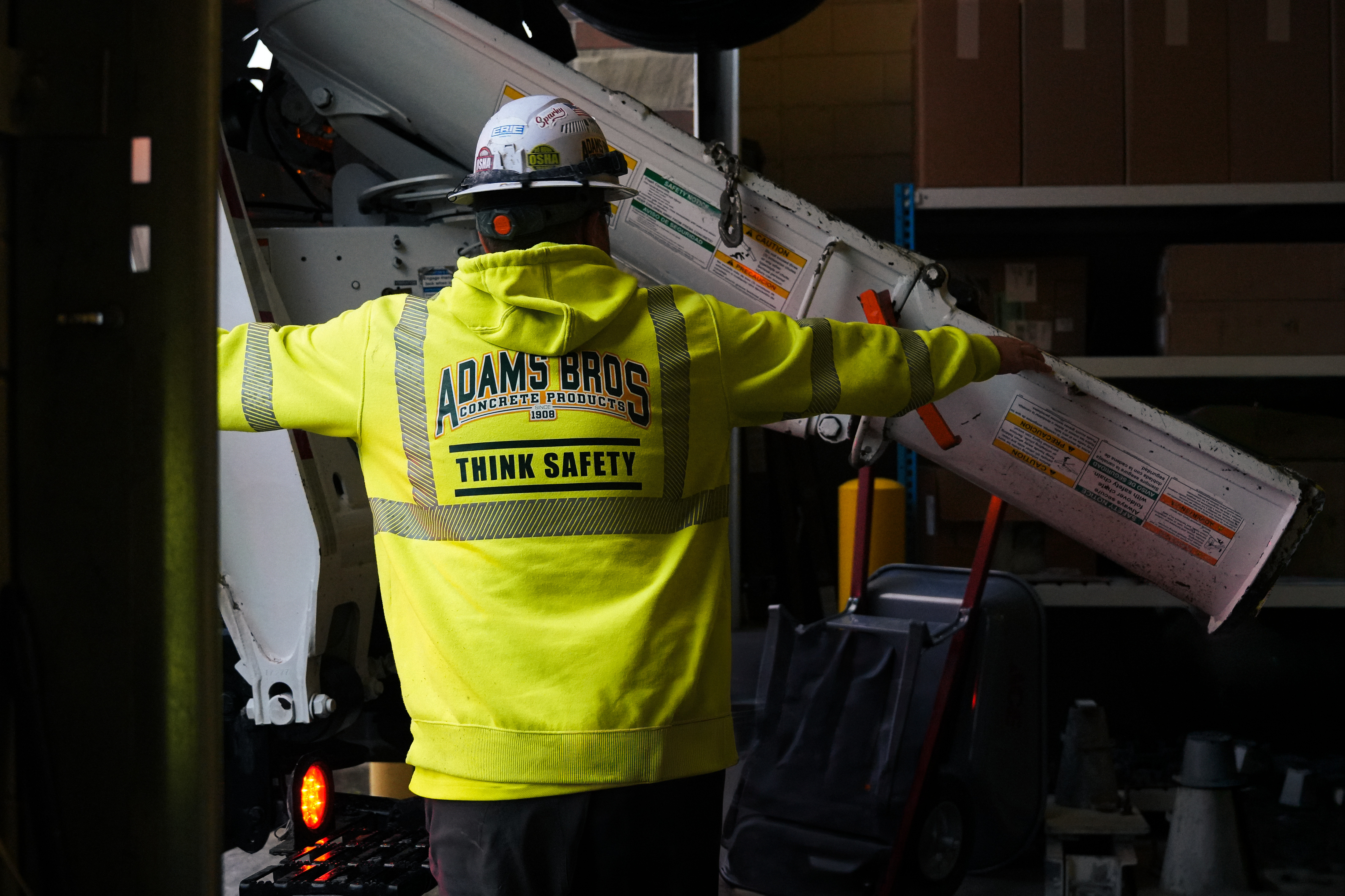 An Adams Bros Concrete Products crew member in a Think Safety hi-vis hoodie and hard hat handling a mixer chute in the shop