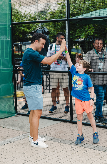 A man and a young boy giving each other a high-five outside near a fenced area, both smiling and enjoying the moment.