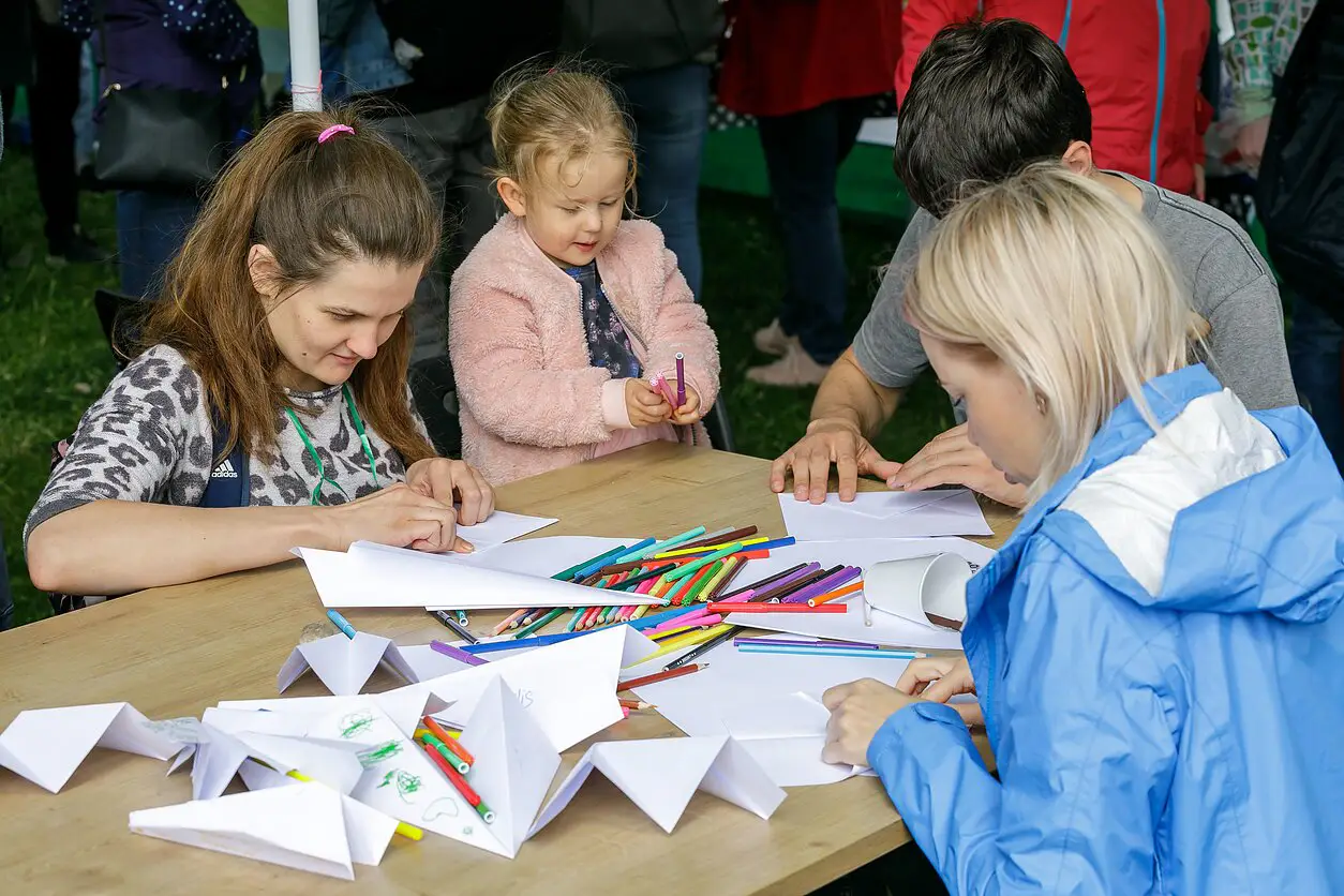 Four people at a table folding paper and using colored pencils for crafts outdoors.