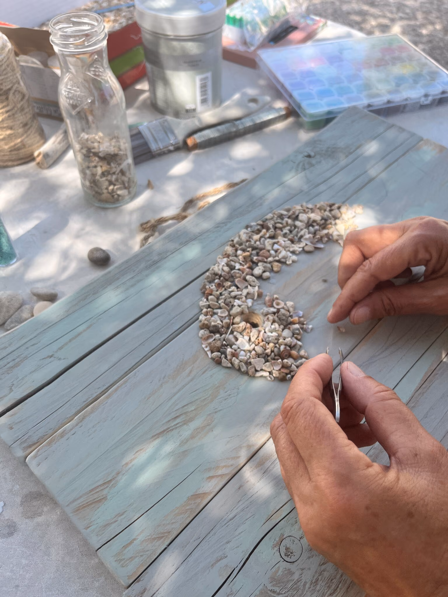 Nens placing sea-worn stones and shells by hand on a reclaimed wooden panel in Puglia