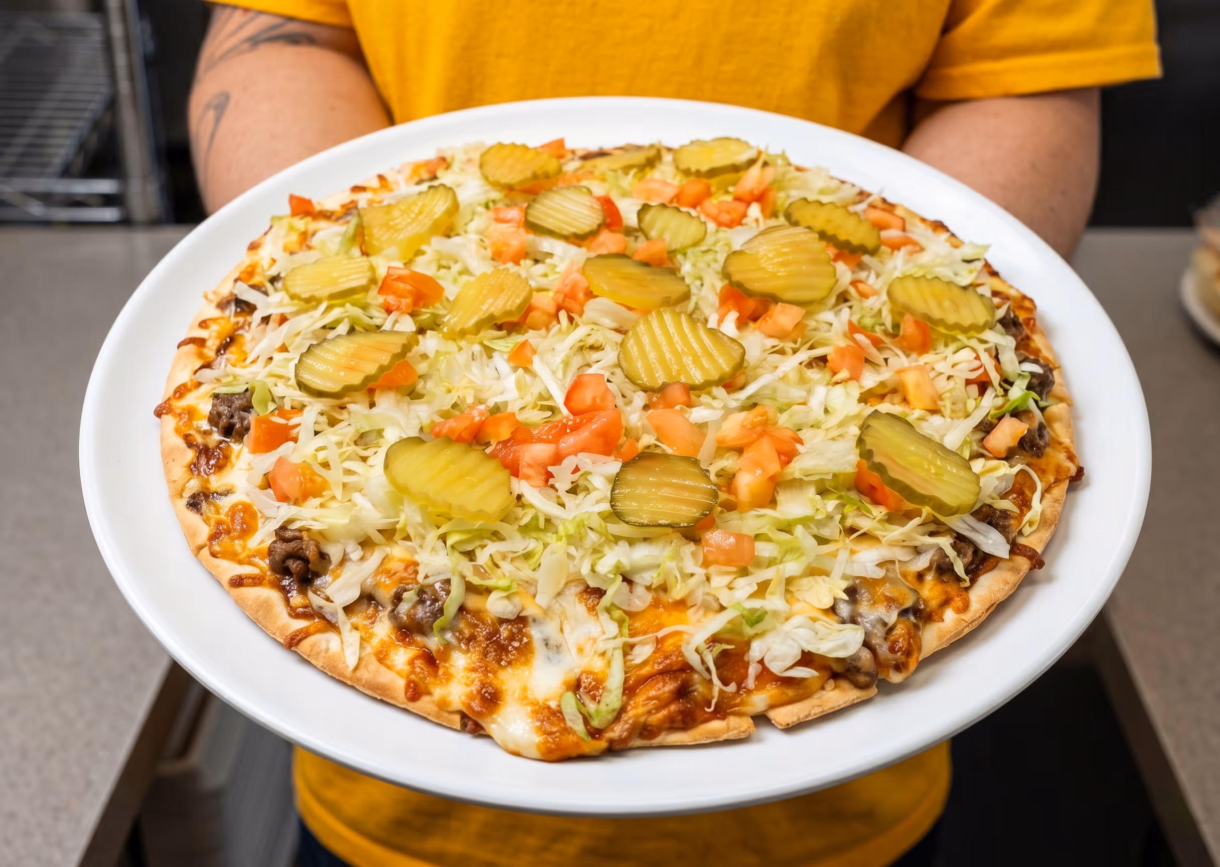 A pizza topped with pickles, lettuce, tomatoes, and ground beef.