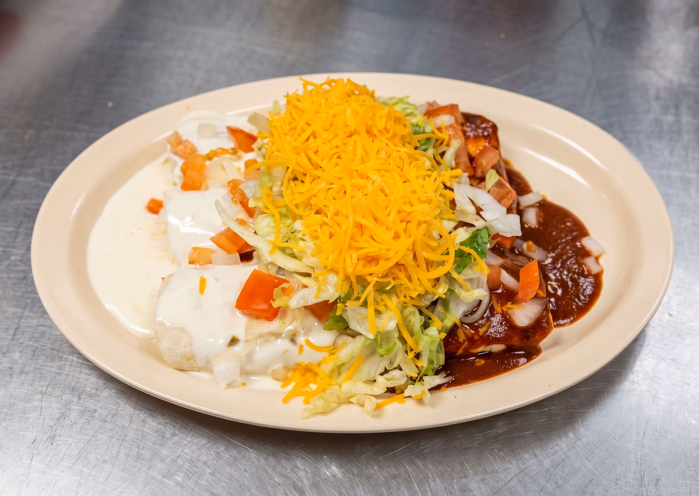 Plate of enchiladas topped with shredded cheese, lettuce, diced tomatoes, onions, and white and red sauces.