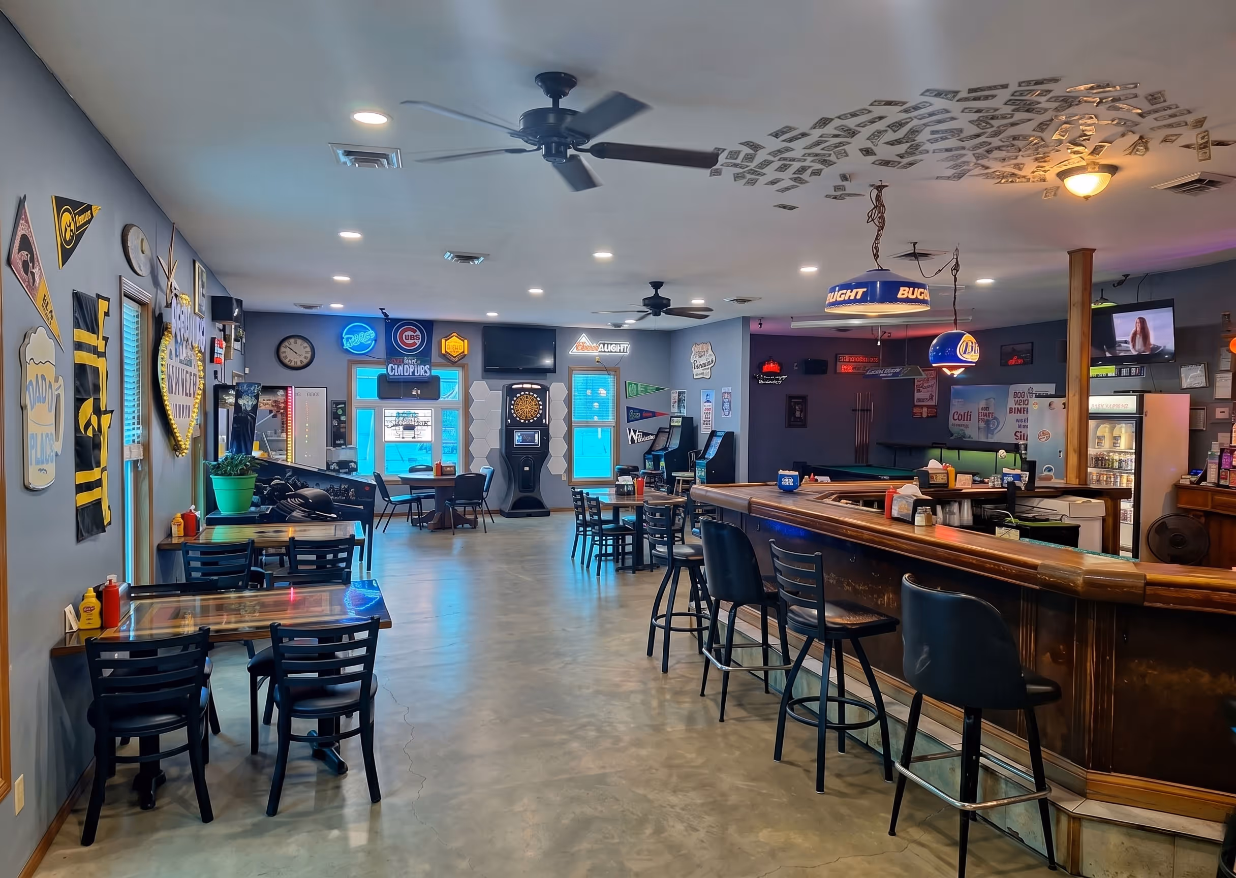 Interior of a bar with tables, bar stools, a dartboard, neon signs, and wall decorations.