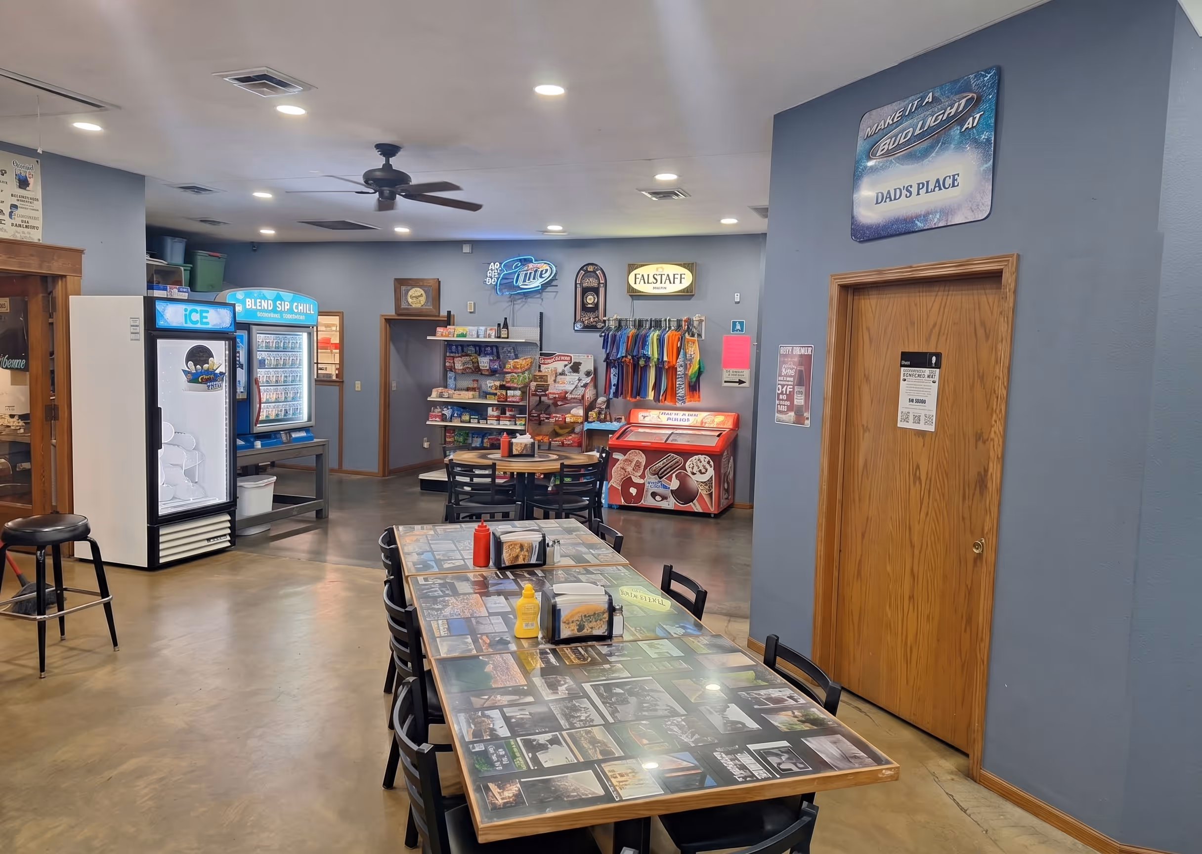 Casual dining area with tables, condiment bottles, beverage coolers, and a wall sign reading Dad's Place.