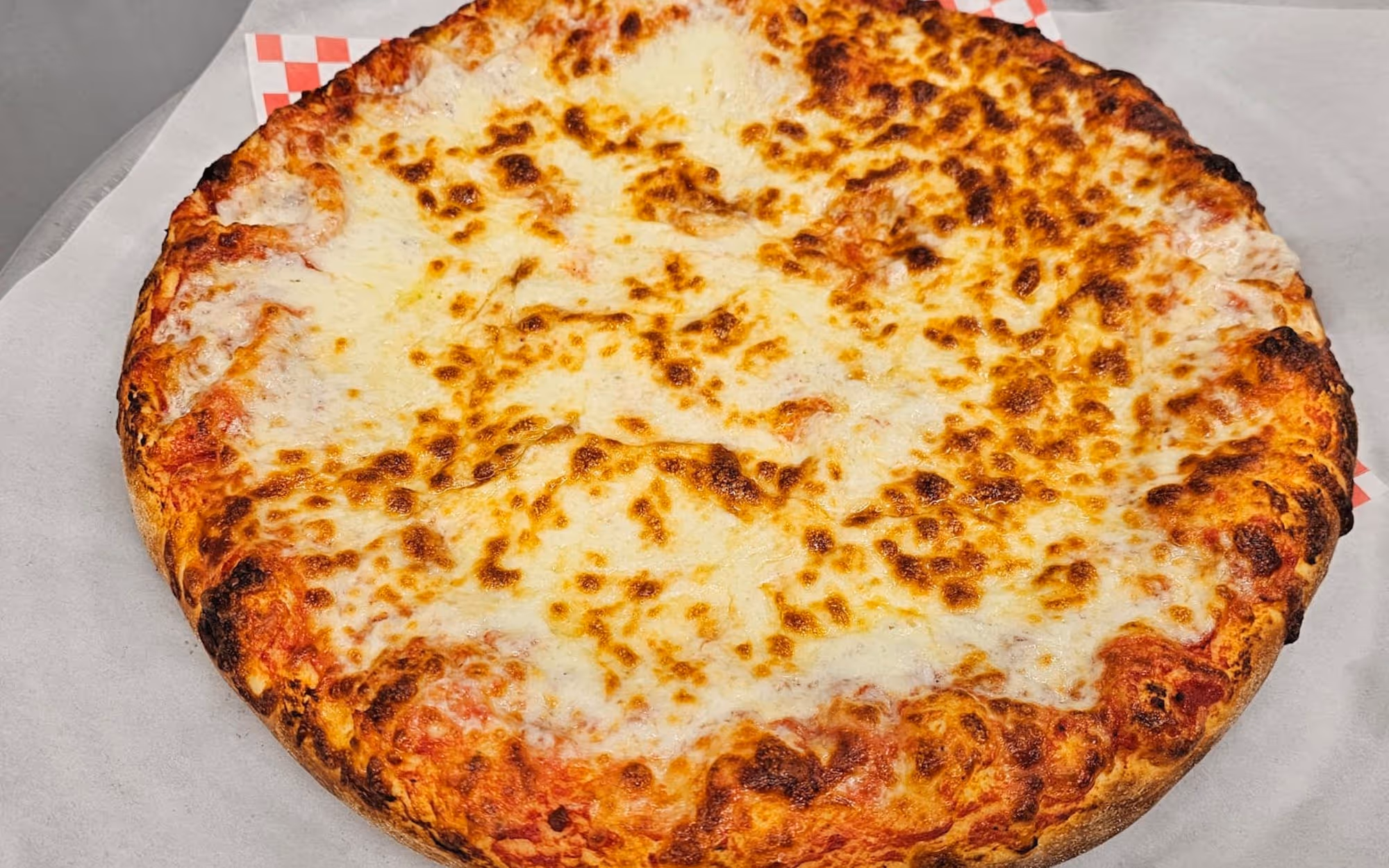 A whole cheese pizza with bubbly, golden-brown mozzarella and a thick, toasted crust on white parchment paper.