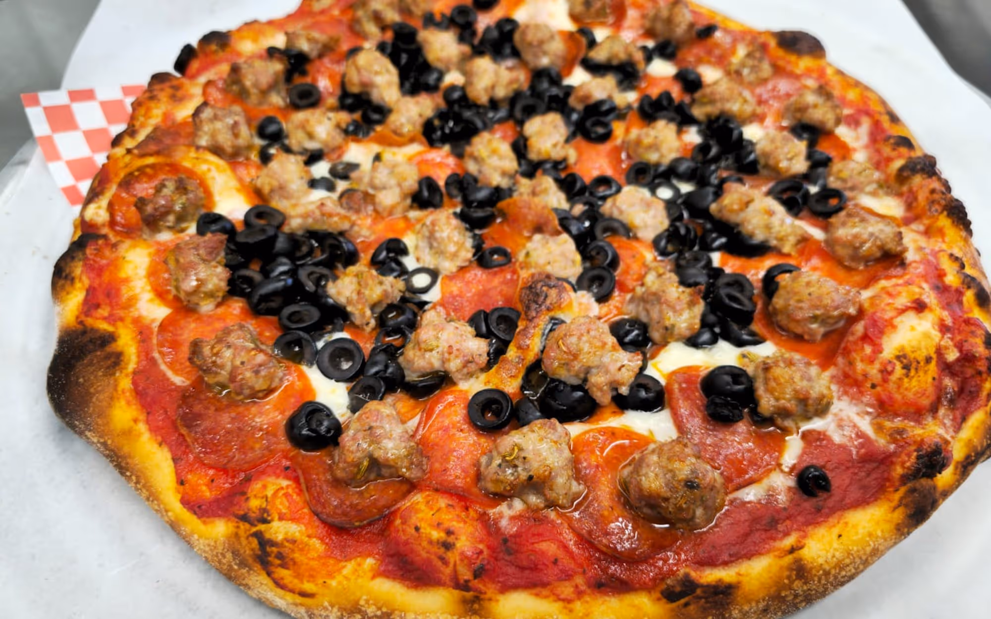 Gourmet pepperoni pizza topped with sliced black olives and large sausage chunks on a crispy thin crust.