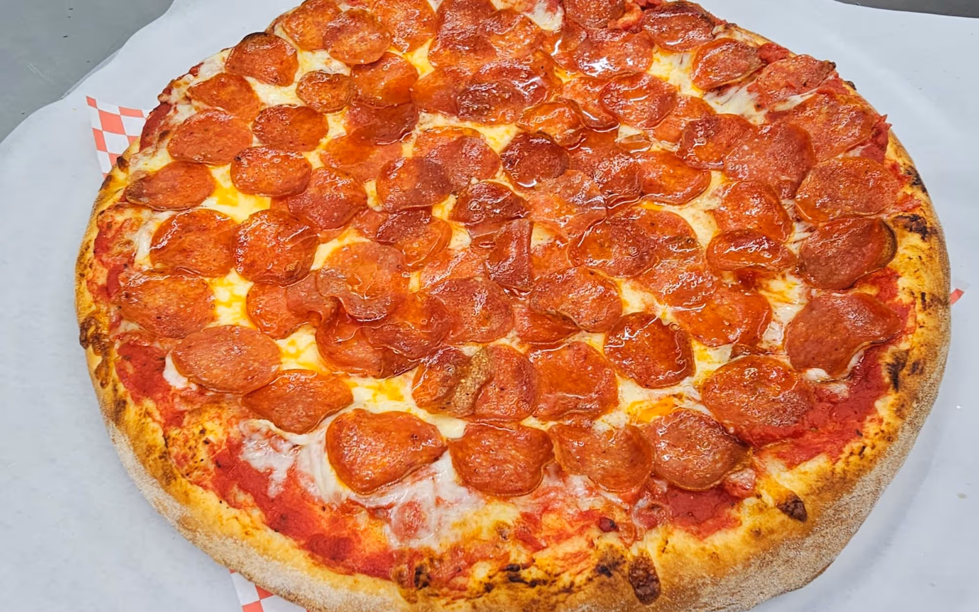 Large New York-style pepperoni pizza with melted mozzarella cheese and crispy crust on white parchment paper.