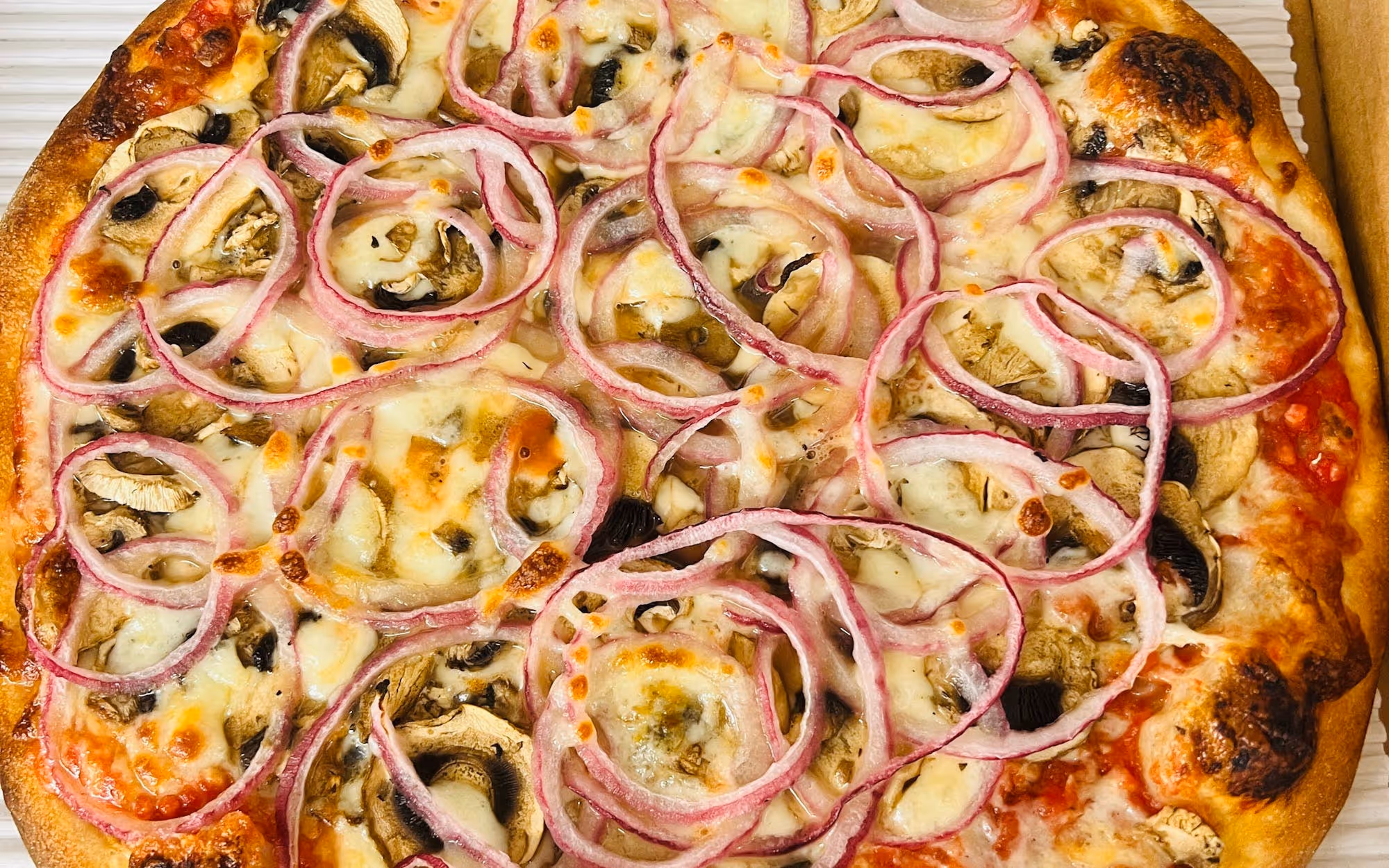 Vegetarian pizza topped with sliced red onions, mushrooms, melted mozzarella cheese, and tomato sauce on a golden crust.