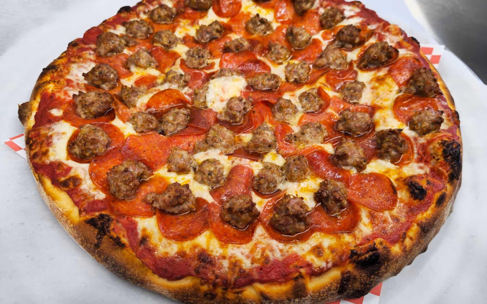 A whole pepperoni and sausage pizza with a golden-brown thin crust, melted mozzarella cheese, and red tomato sauce.