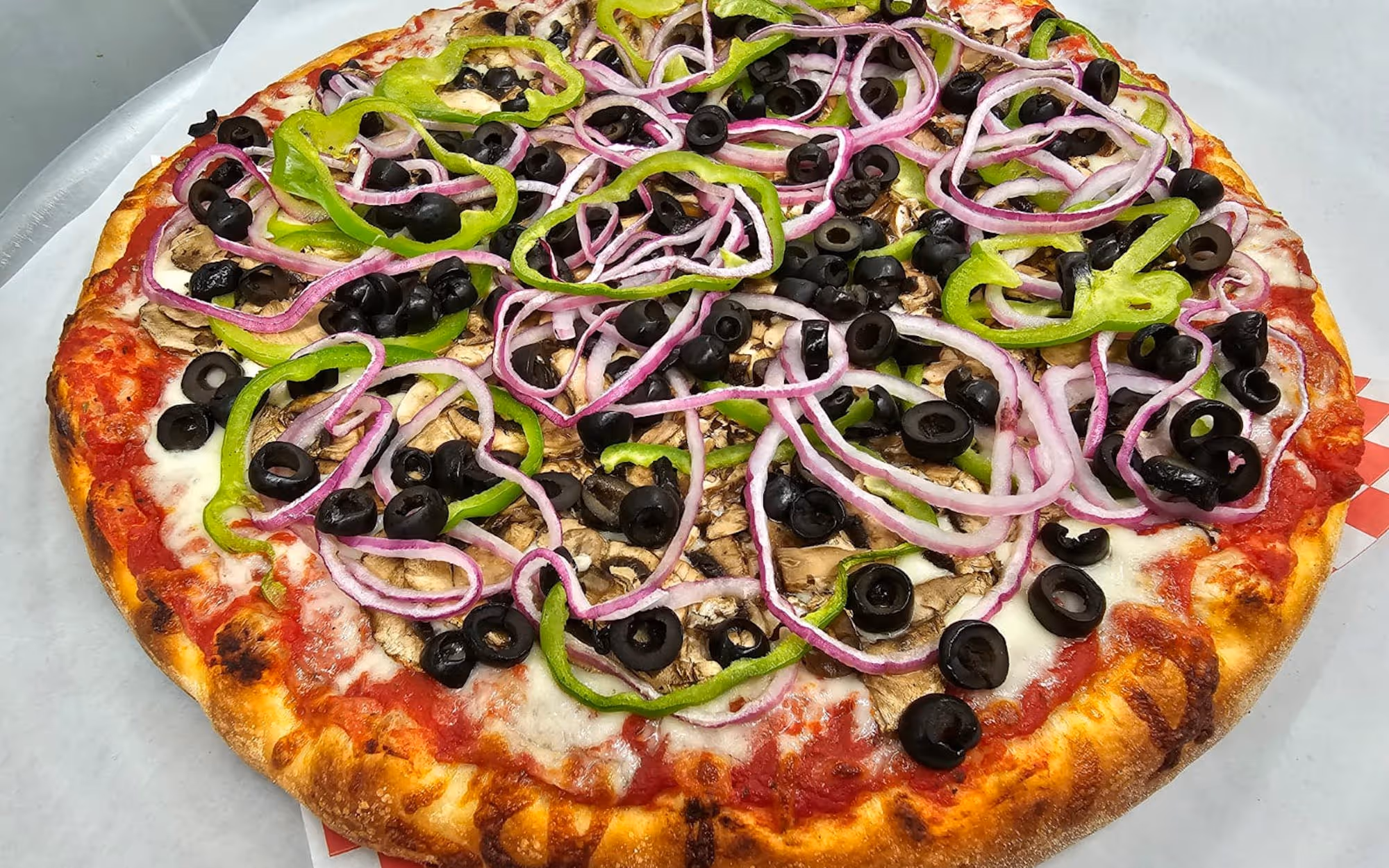 Veggie lover's pizza topped with sliced black olives, red onions, green bell peppers, and mushrooms on a golden crust.