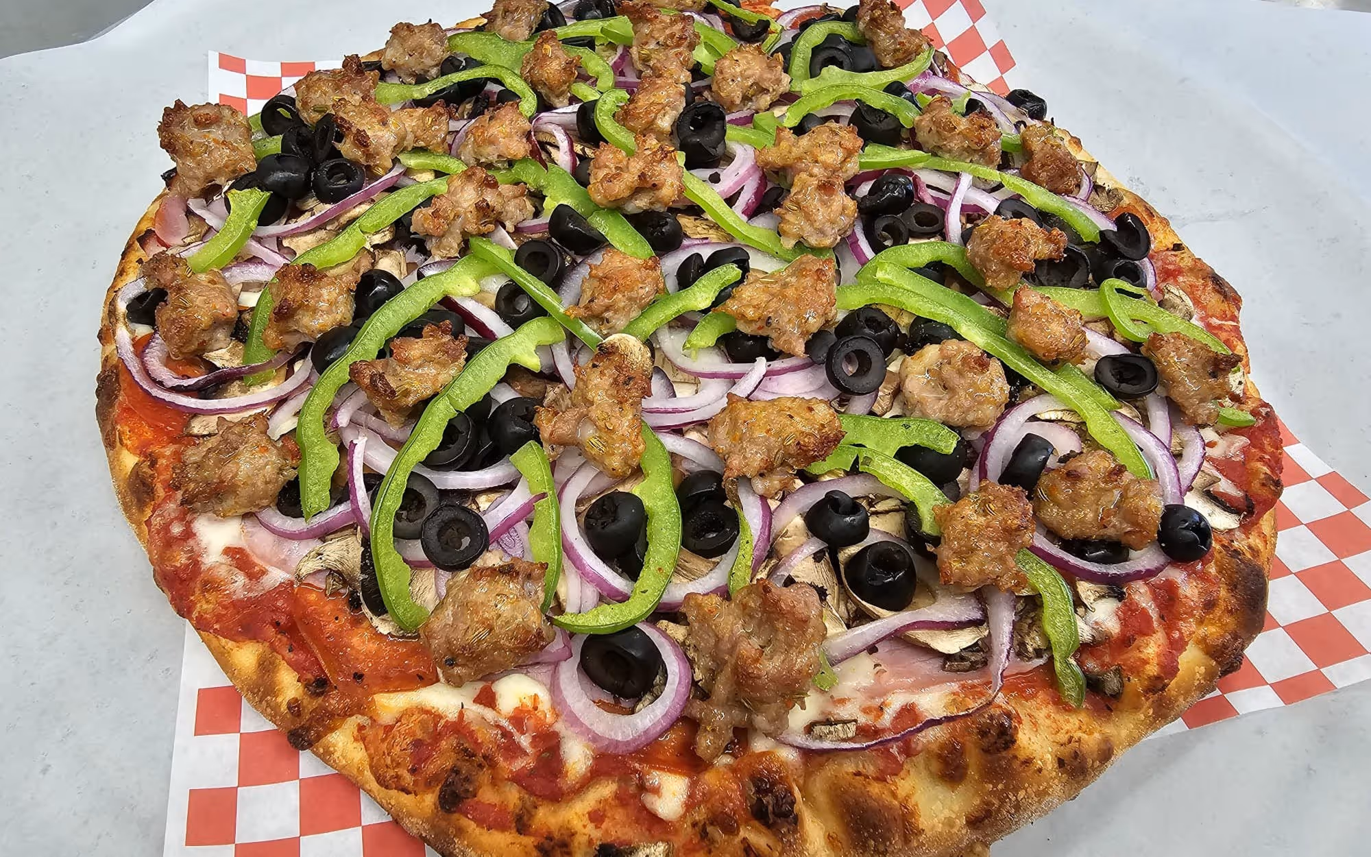 Supreme veggie pizza with red sauce, mozzarella, topped with green bell peppers, red onions, mushrooms, and black olives.