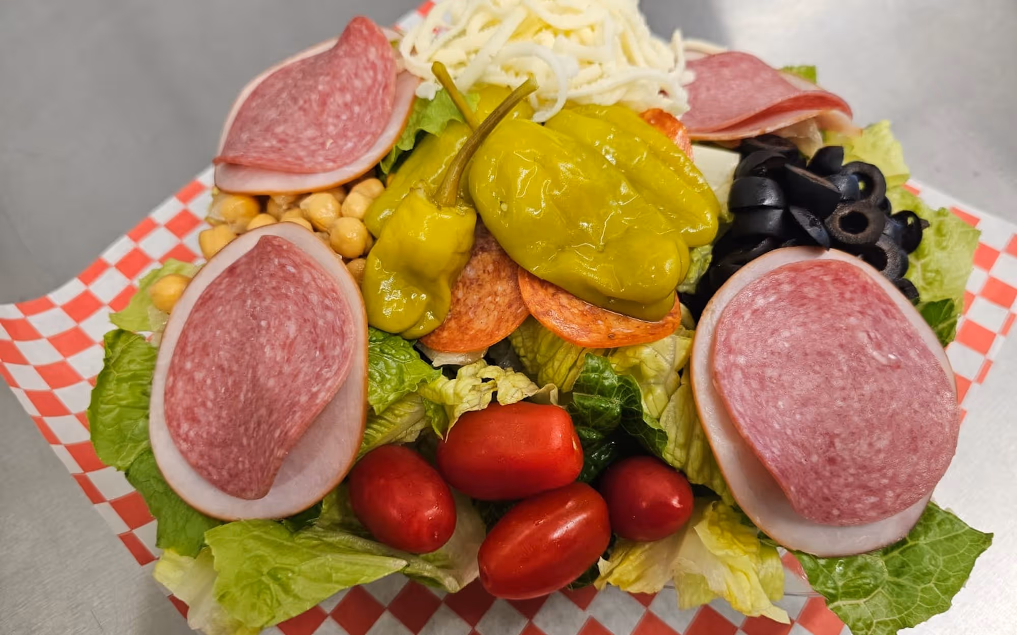 Italian antipasto salad with salami, pepperoni, pepperoncini, tomatoes, black olives, and cheese on a bed of romaine lettuce.