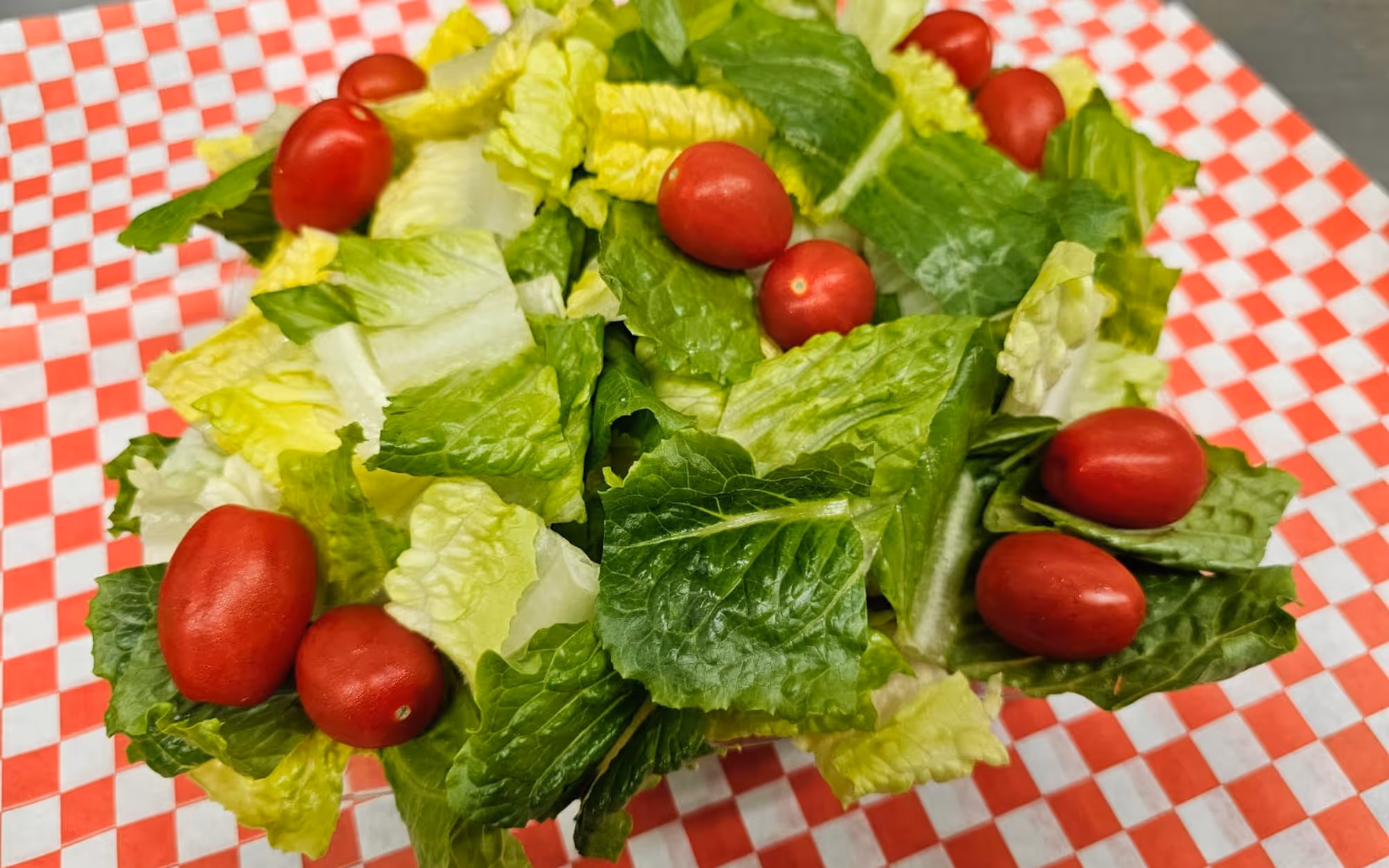 Fresh garden salad with crisp romaine lettuce and red grape tomatoes on a red and white checkered paper liner.