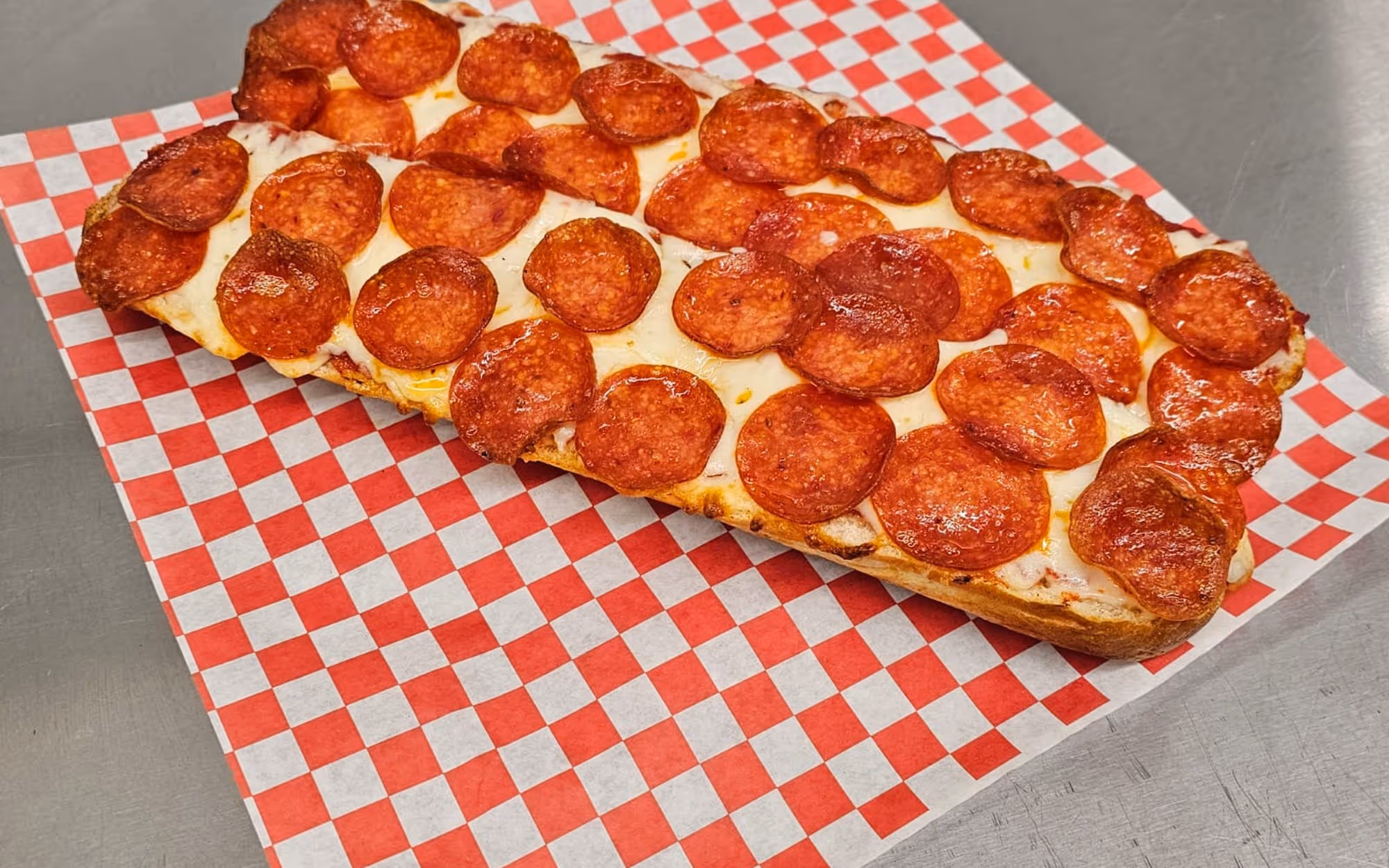 Pepperoni French bread pizza with melted cheese on a red and white checkered deli paper.