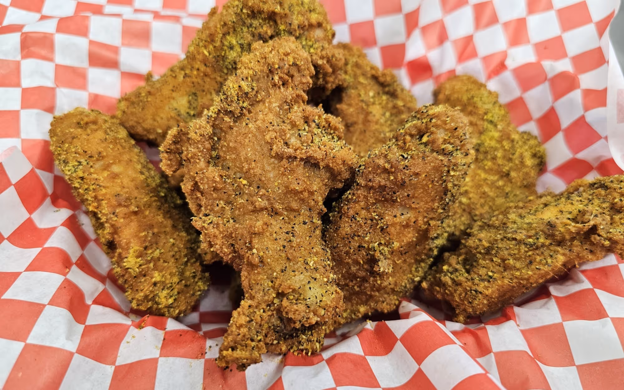 Lemon pepper chicken wings with crispy golden-brown breading in a red and white checkered basket liner.