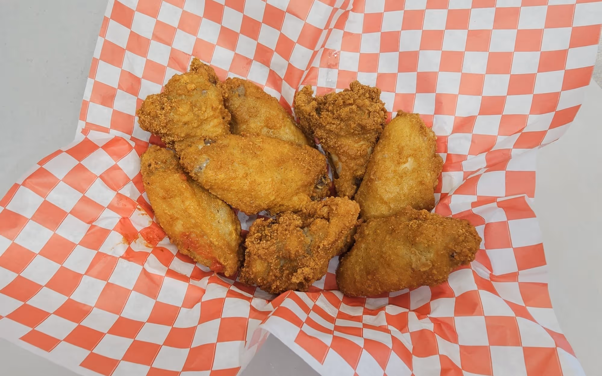 Crispy fried chicken wings served in a basket with red and white checkered deli paper.