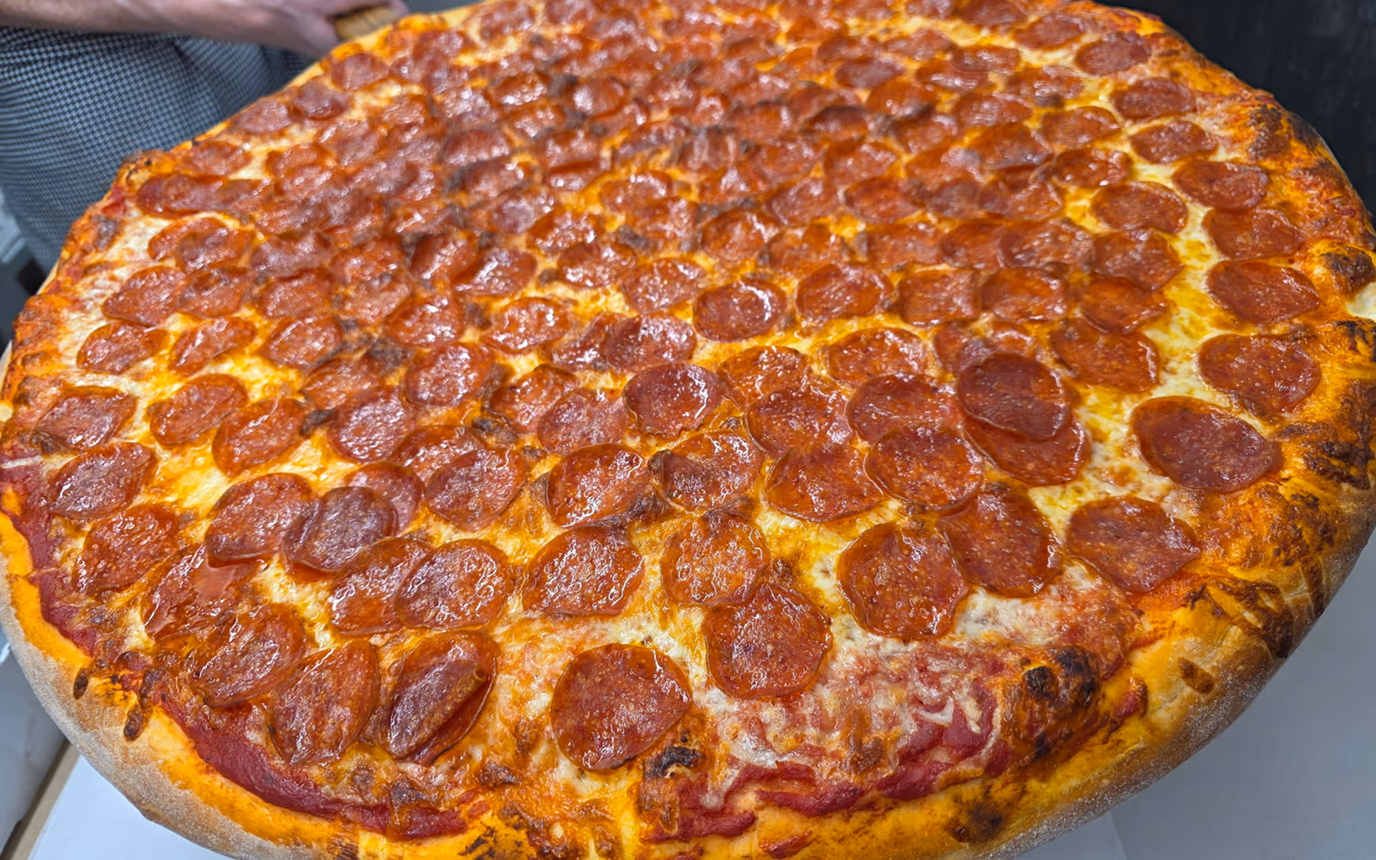 Large pepperoni pizza with thin, crispy crust and melted mozzarella cheese, heavily topped with round pepperoni slices.