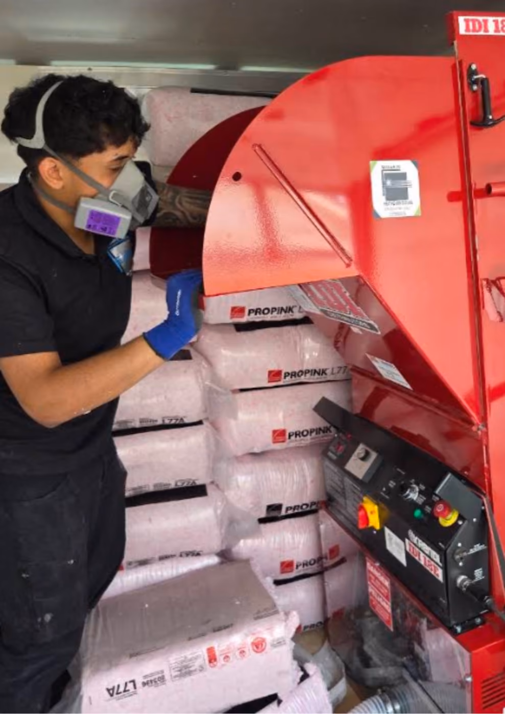 Technician in a respirator loading insulation bags into the blowing machine.
