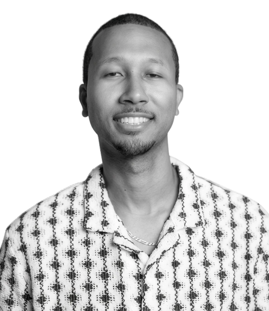 Black-and-white portrait of a smiling man wearing a patterned shirt and chain necklace against a bright yellow background.