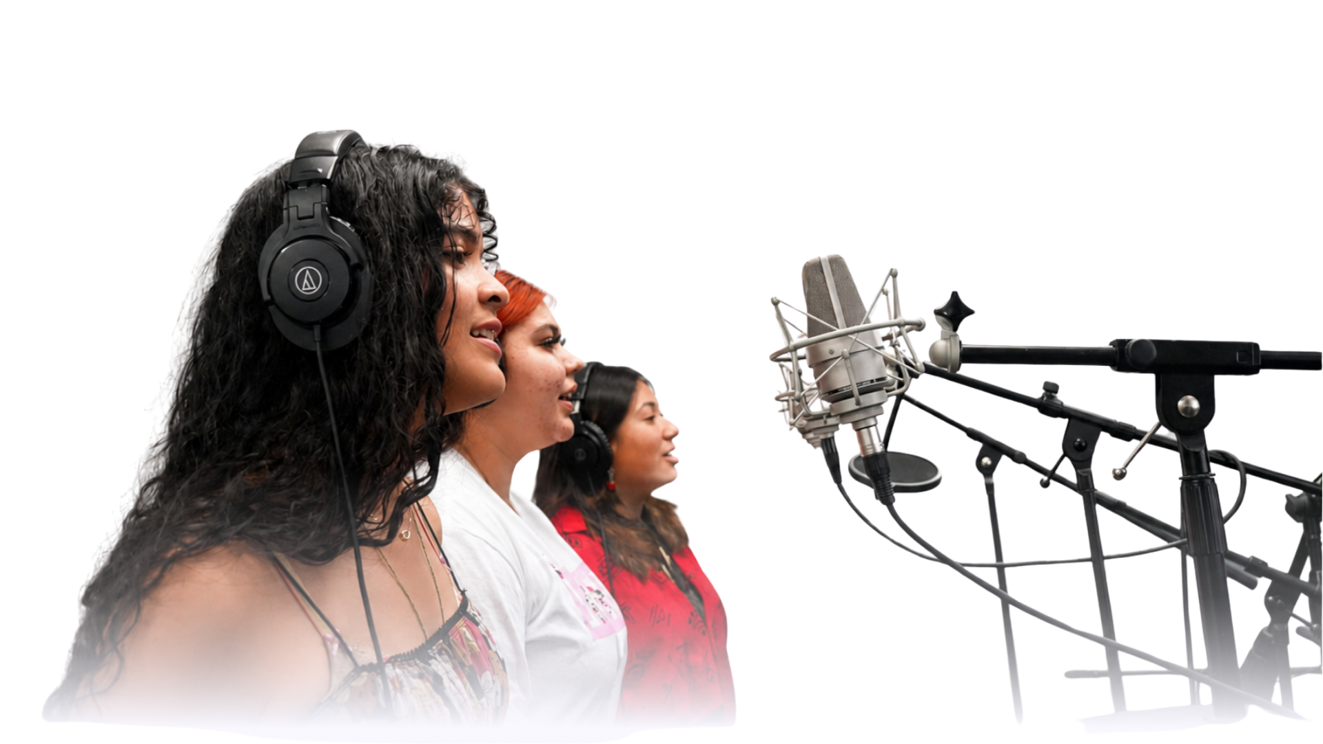 Three women wearing headphones sing into studio microphones during a music recording session.