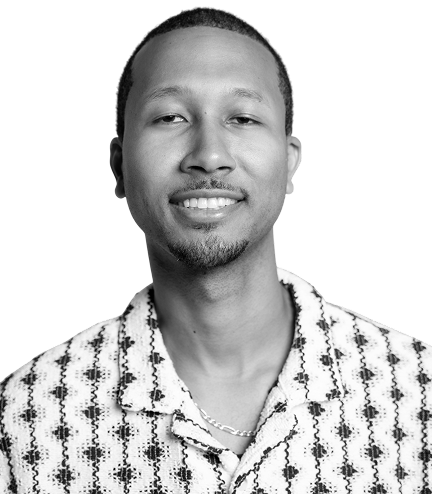Black-and-white portrait of a smiling man wearing a patterned shirt and chain necklace against a bright yellow background.