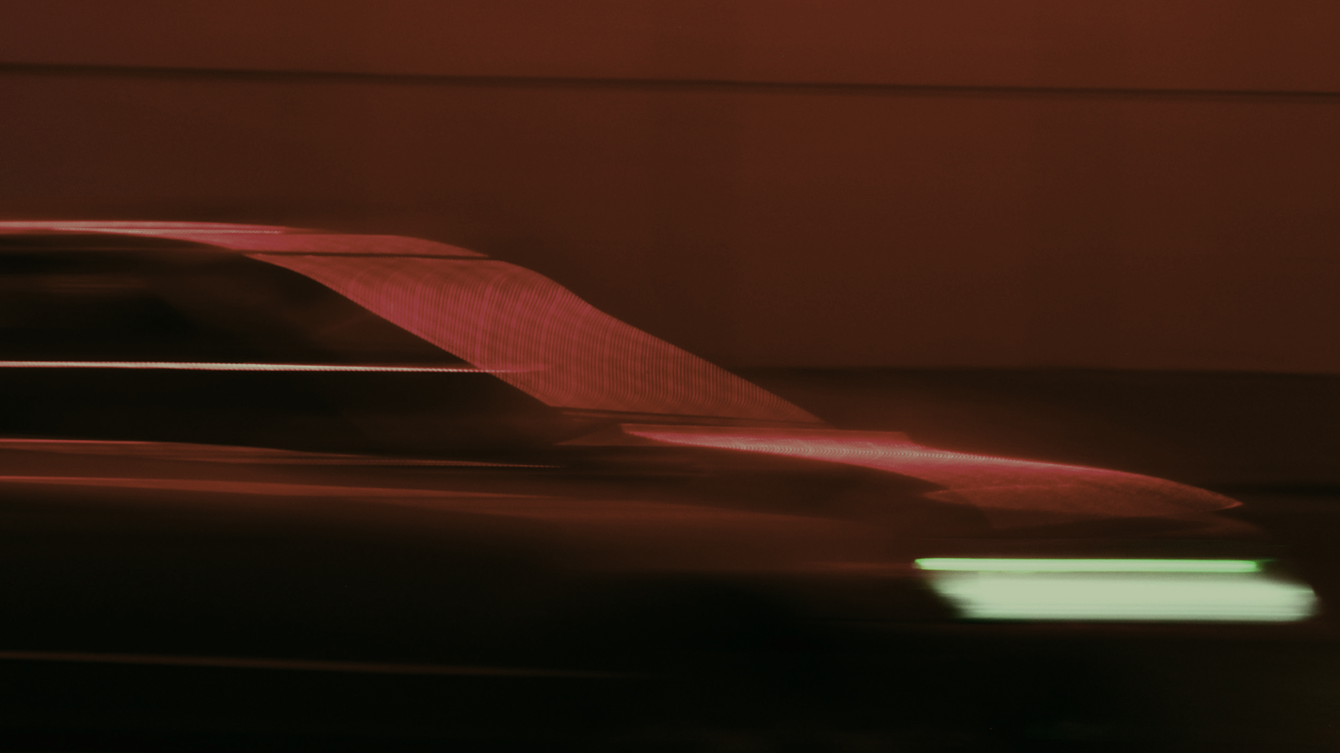 Blurred side view of a moving car with red and green lights on a dark background.