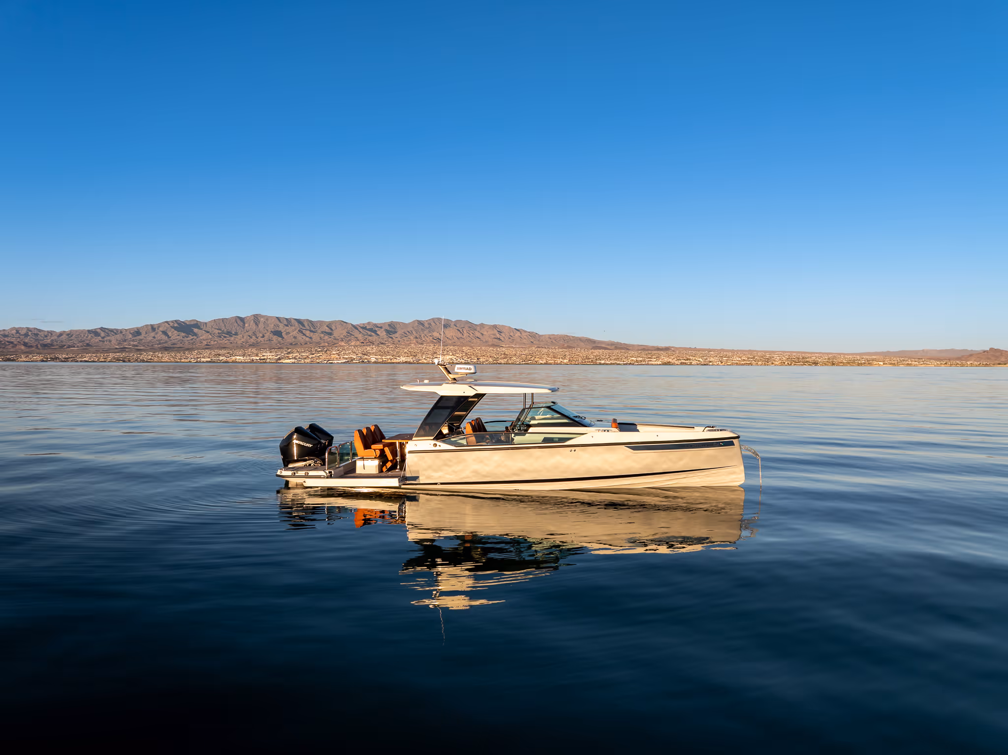Modern beige motorboat with orange seats floating on calm water with distant mountain range background.