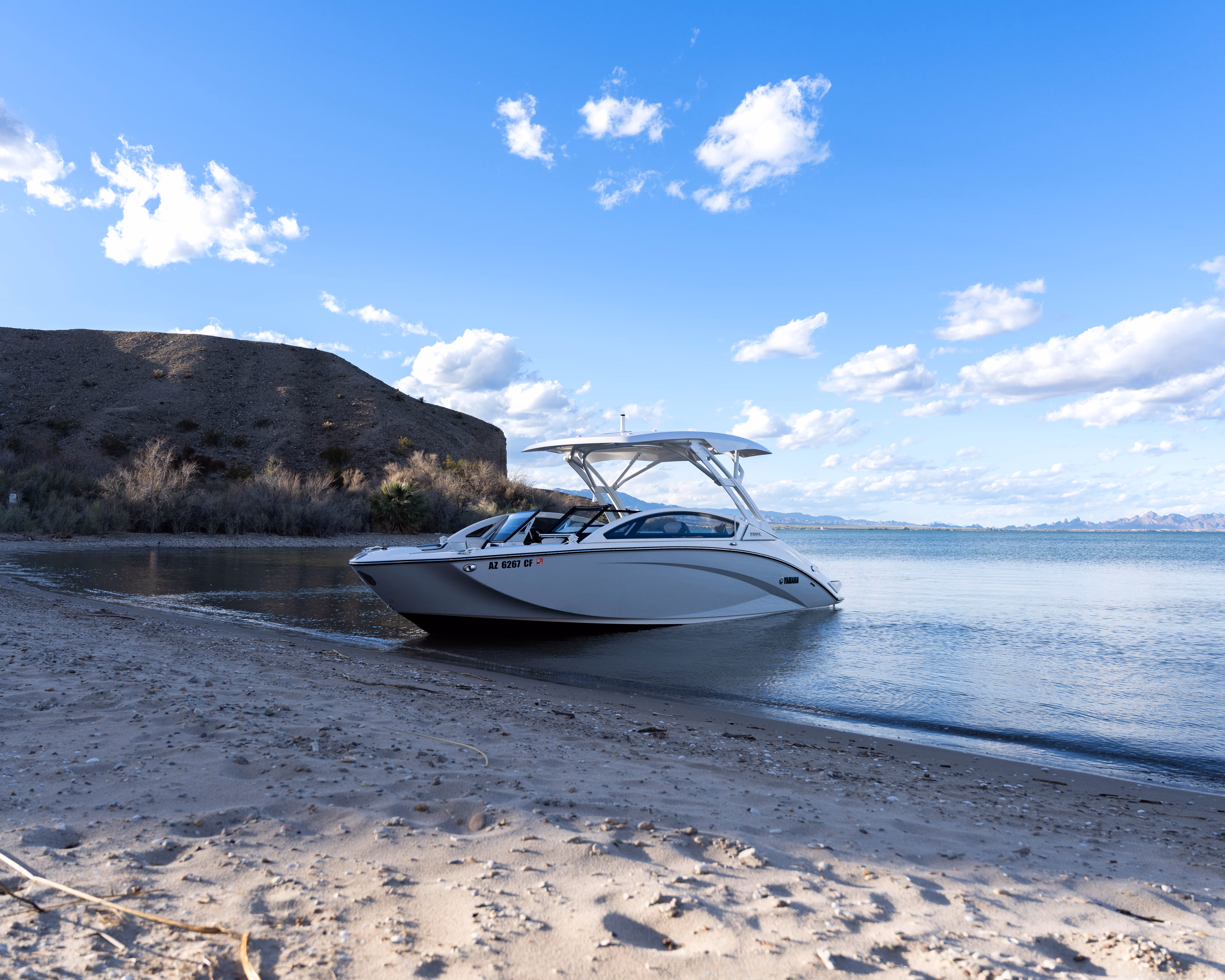 White motorboat docked on a sandy beach with hills and blue sky in the background.
