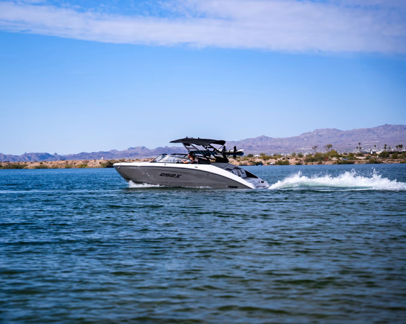 White and black speedboat cruising on a lake with mountains and clear sky in the background.