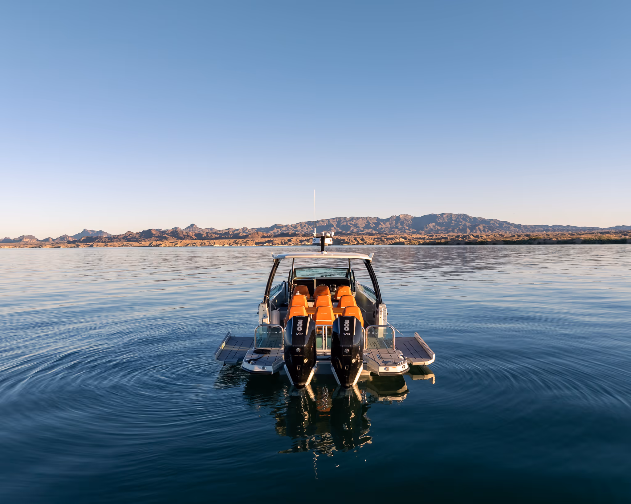 Rear view of a boat with orange seats on calm water with mountains under clear blue sky.