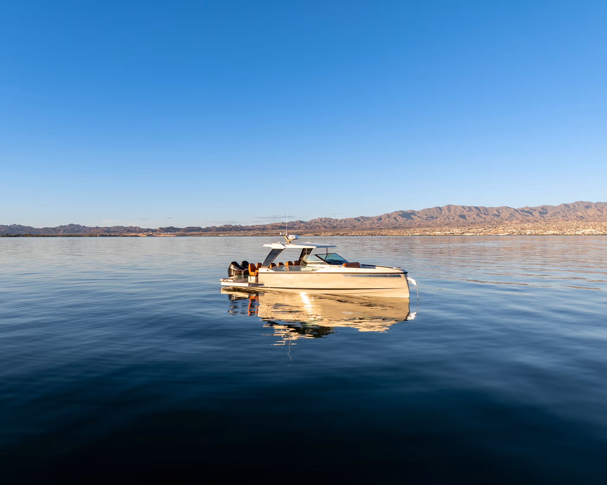 Modern white motorboat floating on calm water with mountain range in the background under clear sky.