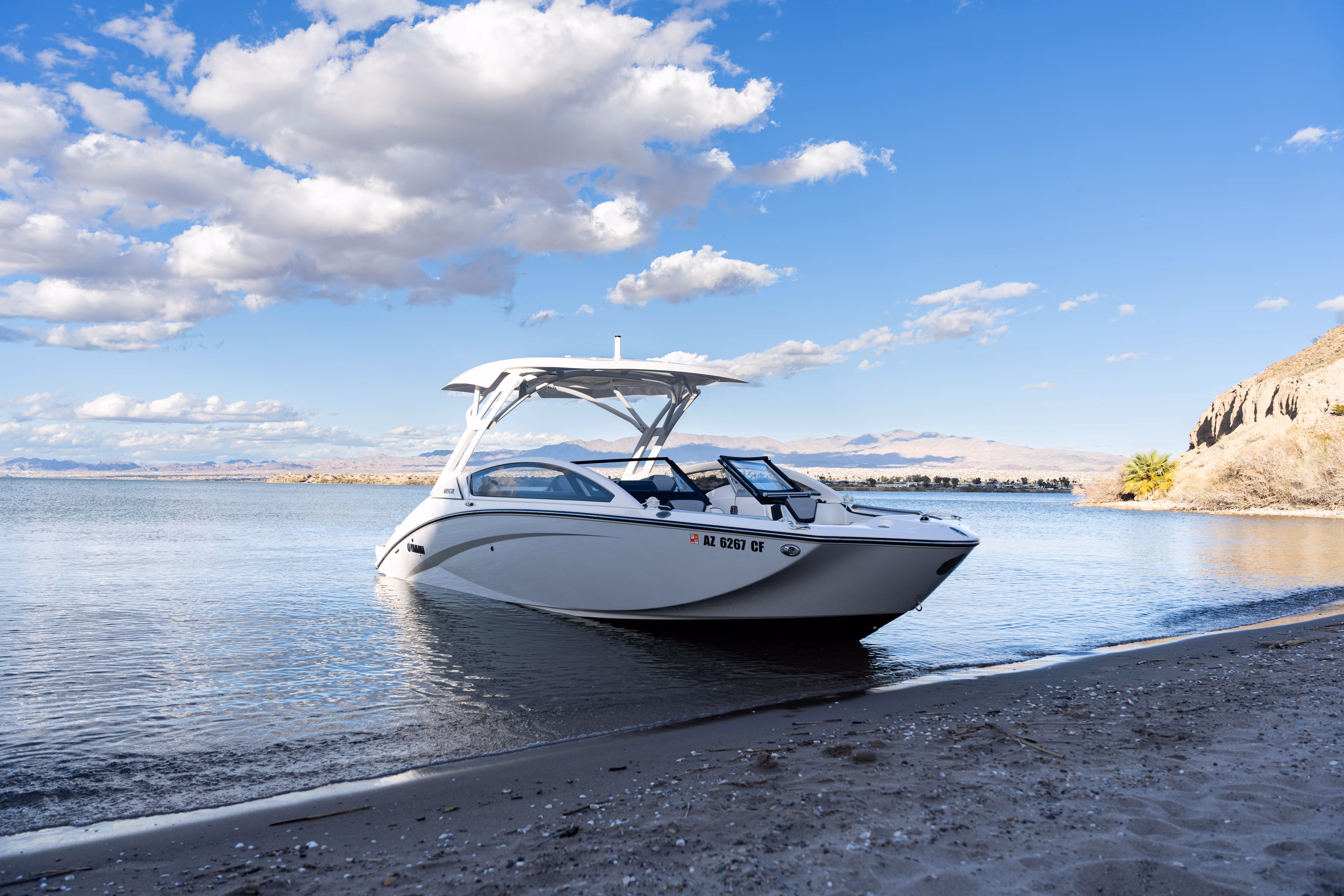 White motorboat anchored near a sandy shore with mountains and clouds in the background.