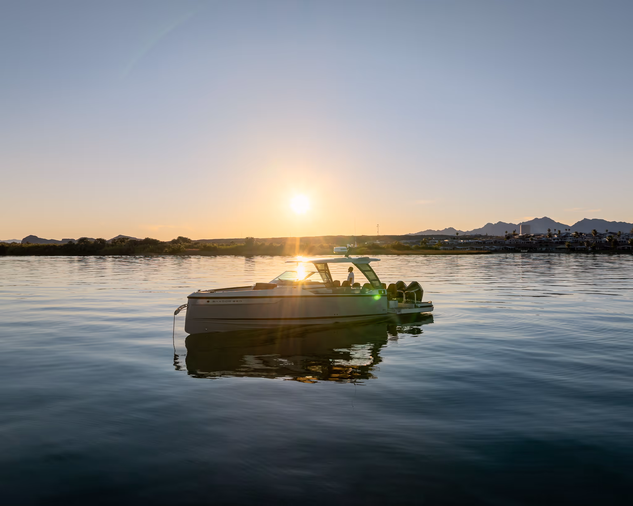 Boat floating on calm water at sunset with mountains and buildings in the background.