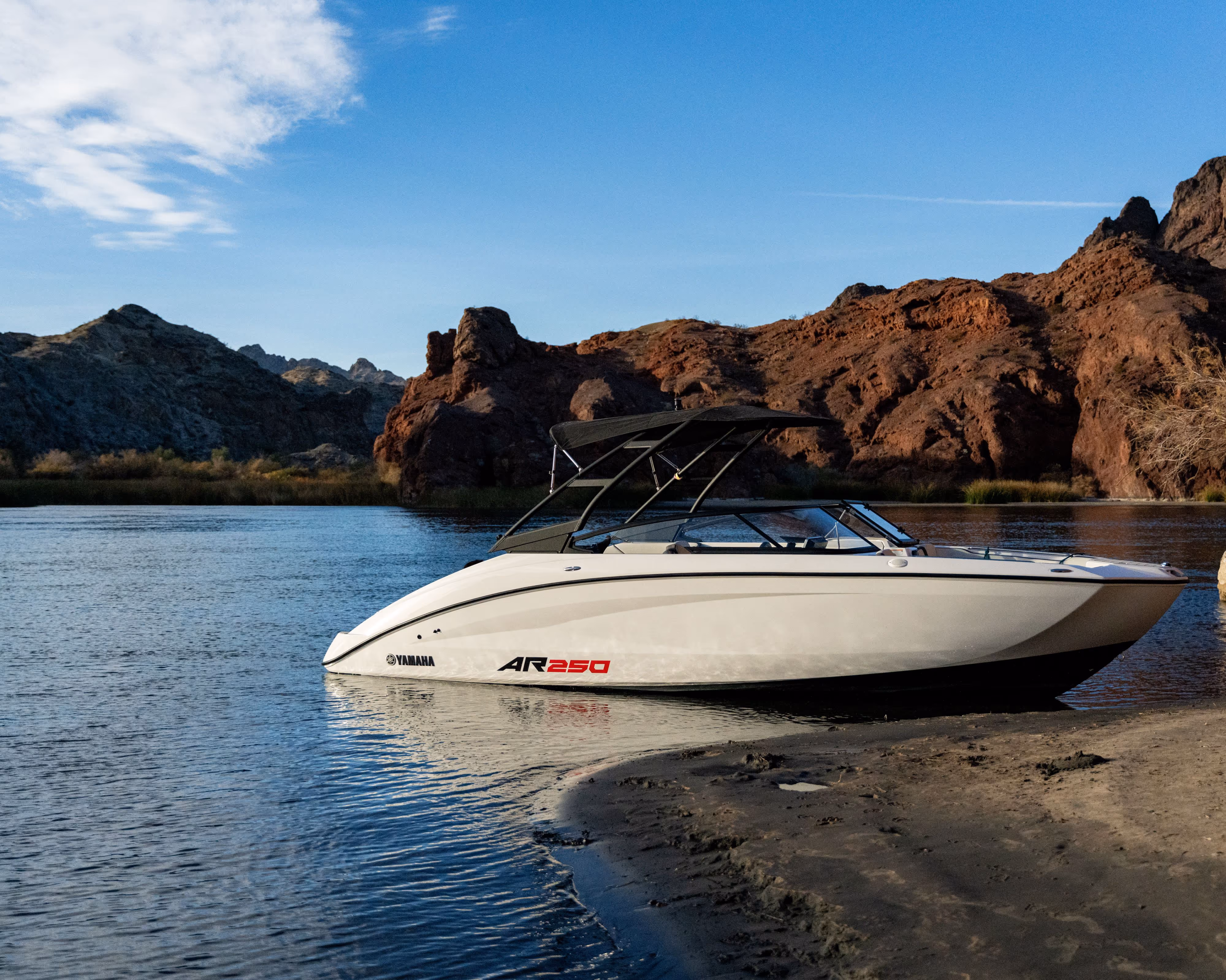 White Yamaha AR250 speedboat near the sandy shore with rocky hills under a blue sky.
