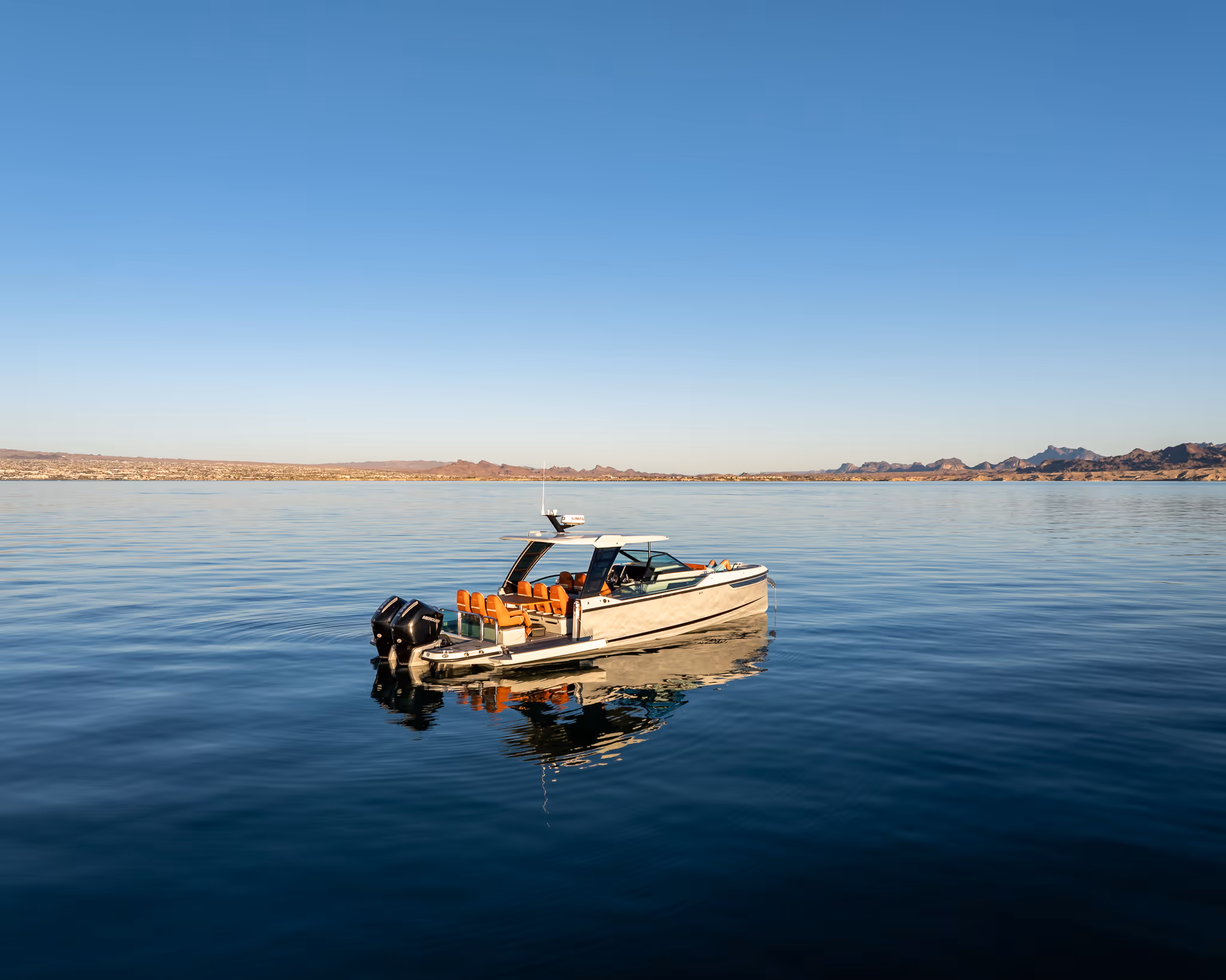 Modern motorboat with orange seats floating on calm water near rocky shore under clear sky.