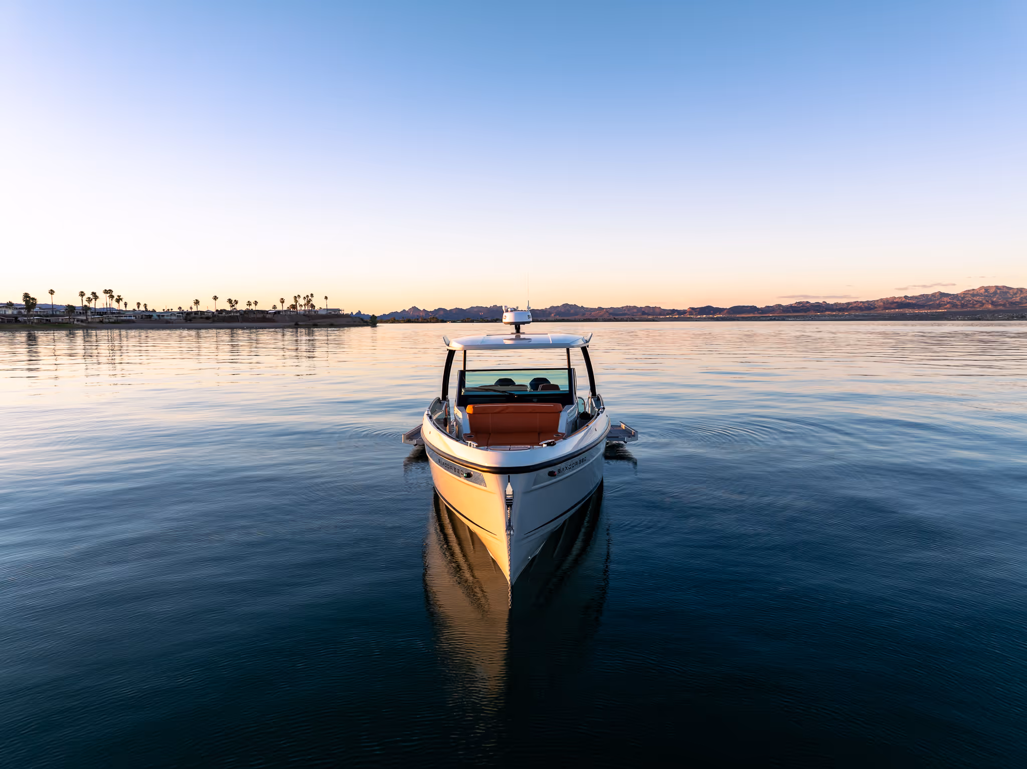 White boat with orange seats floating on calm water at sunset with distant shore and mountains.