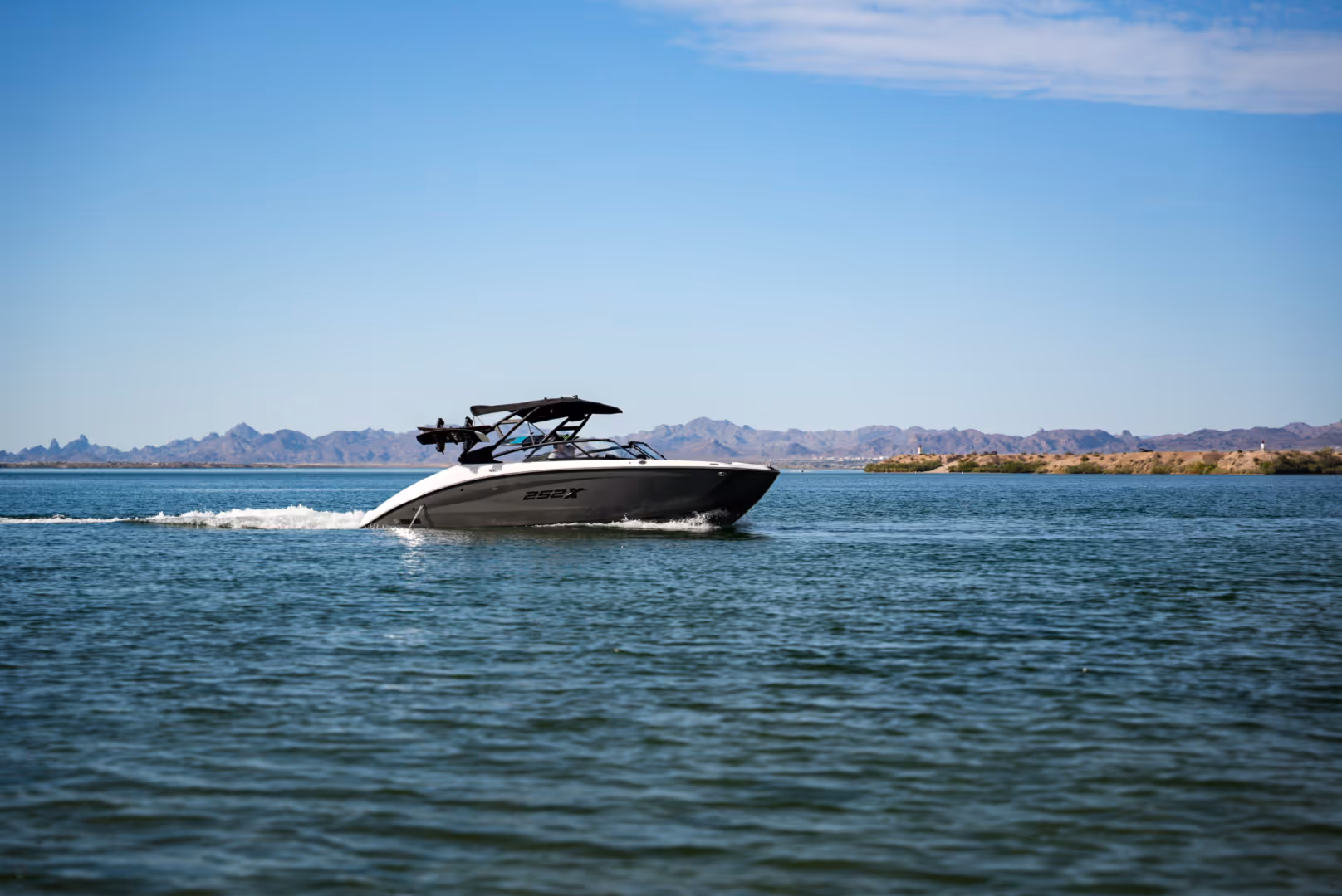 White and black motorboat cruising on calm water with mountains and clear sky background.