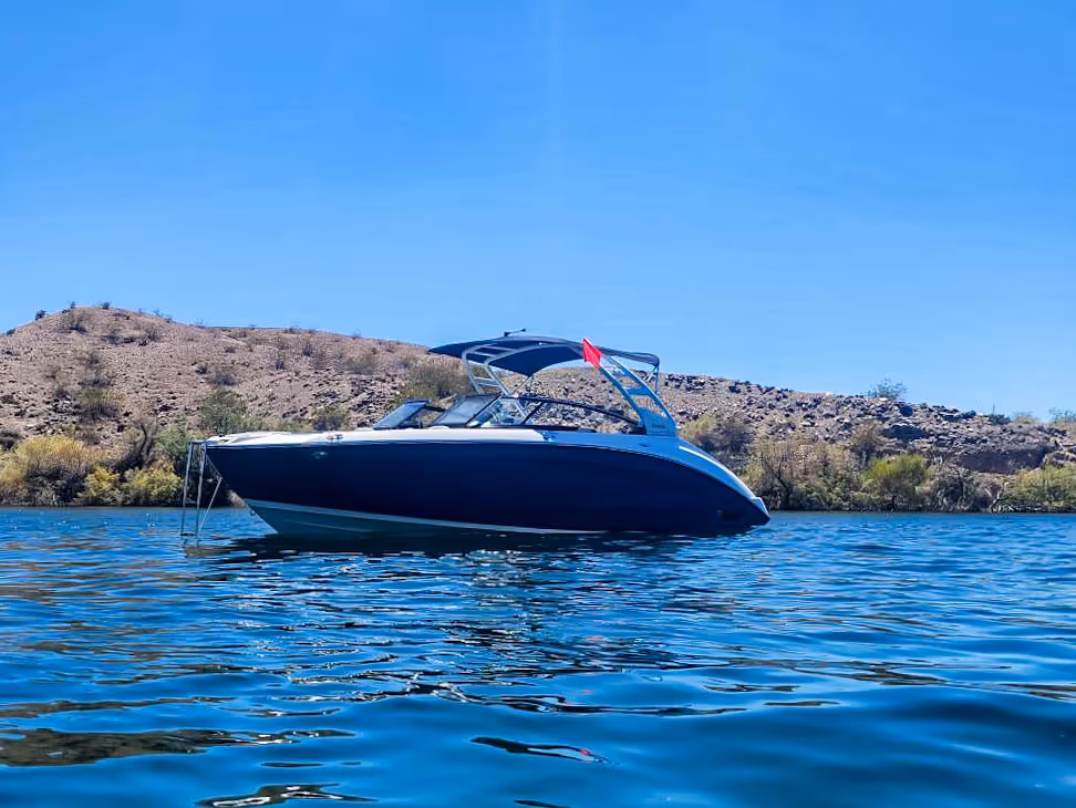 Blue and white motorboat floating on calm water with hills and clear blue sky in the background.