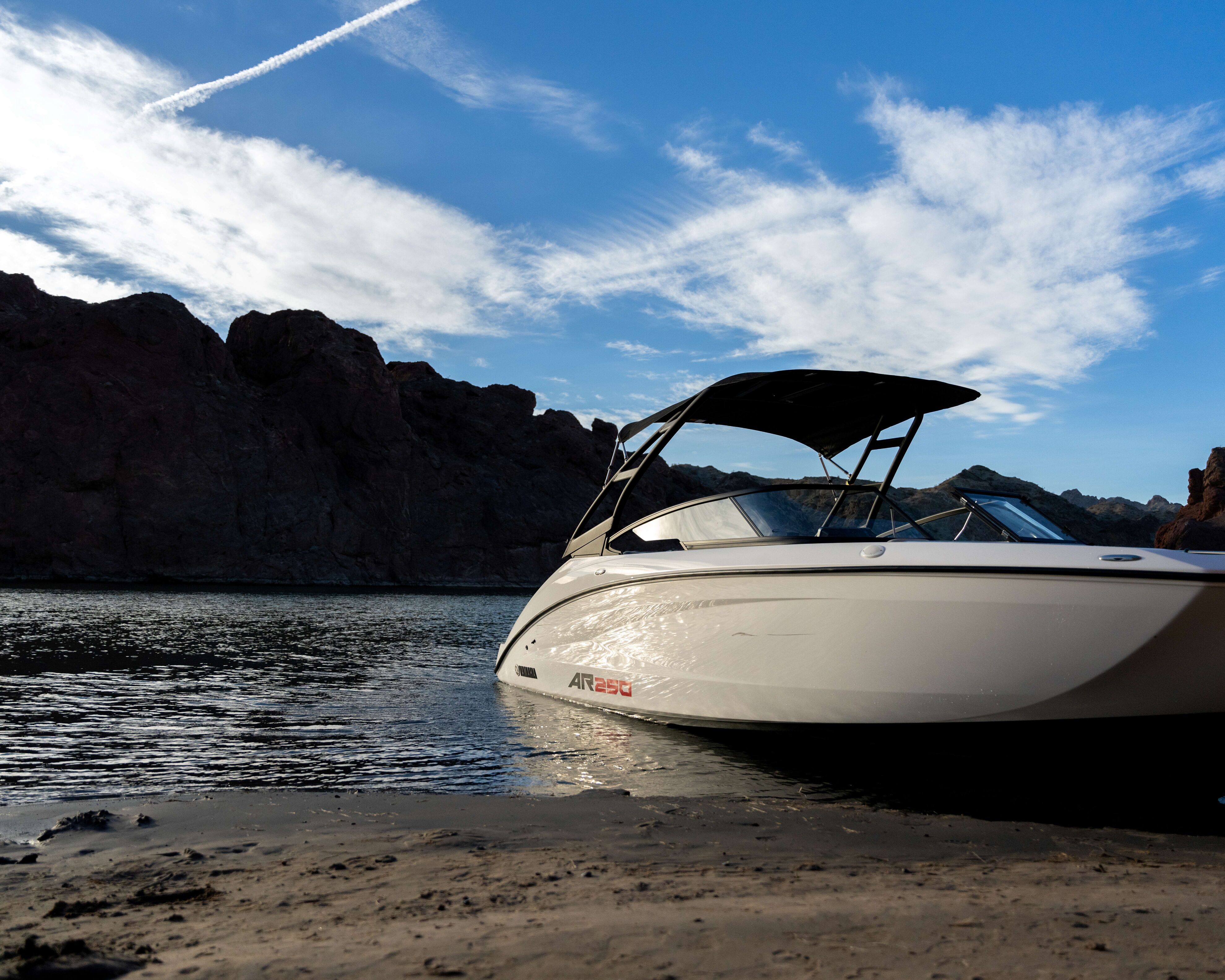 White motorboat with black canopy docked on a sandy shore with rocky hills in the background.