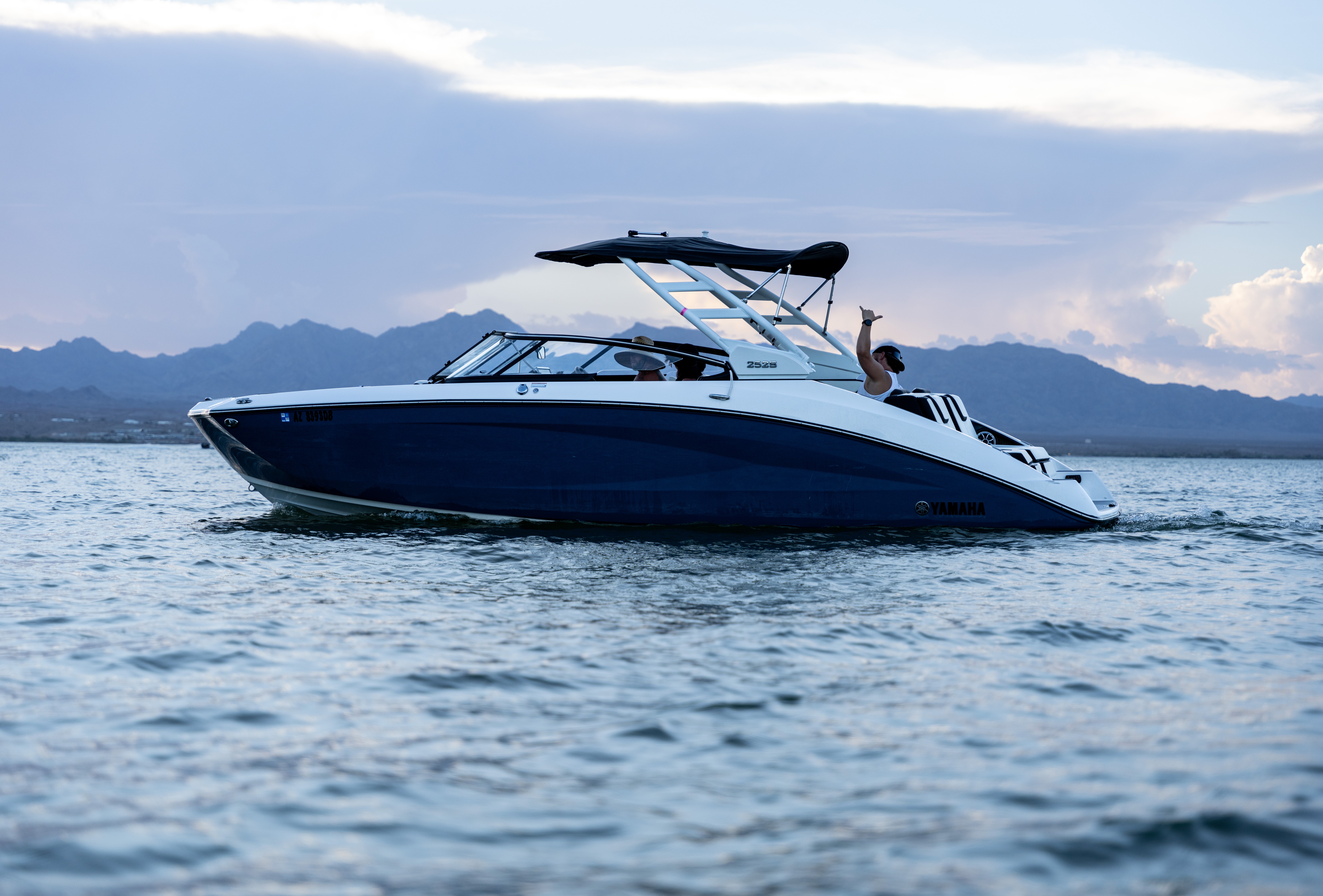 Blue and white Yamaha speedboat on water with three people and mountain range in background.
