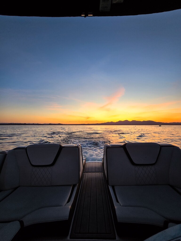 View from boat seats looking toward water and a colorful sunset with mountains on the horizon.