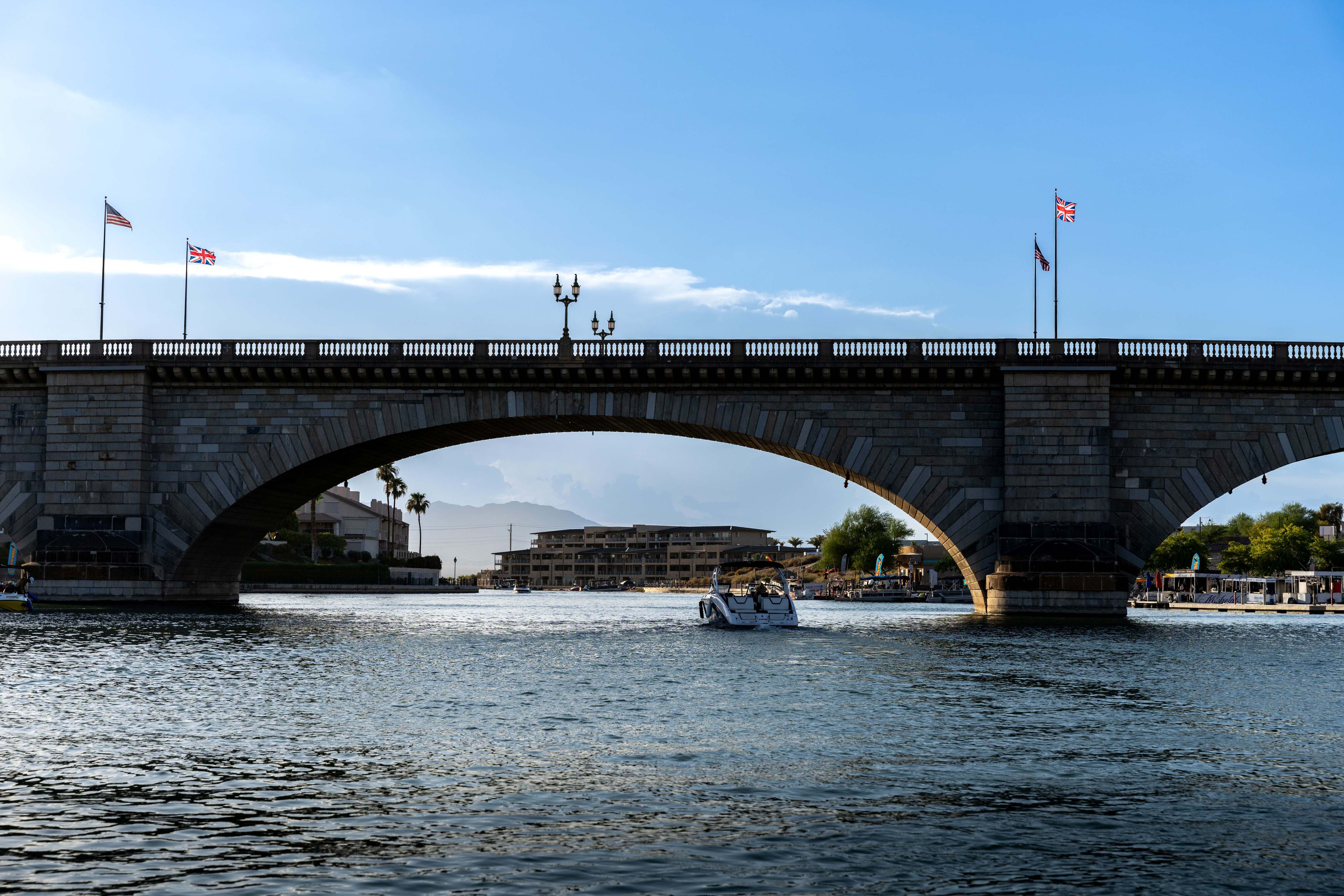 Boat passing under a stone arch bridge with American and British flags on poles above it.