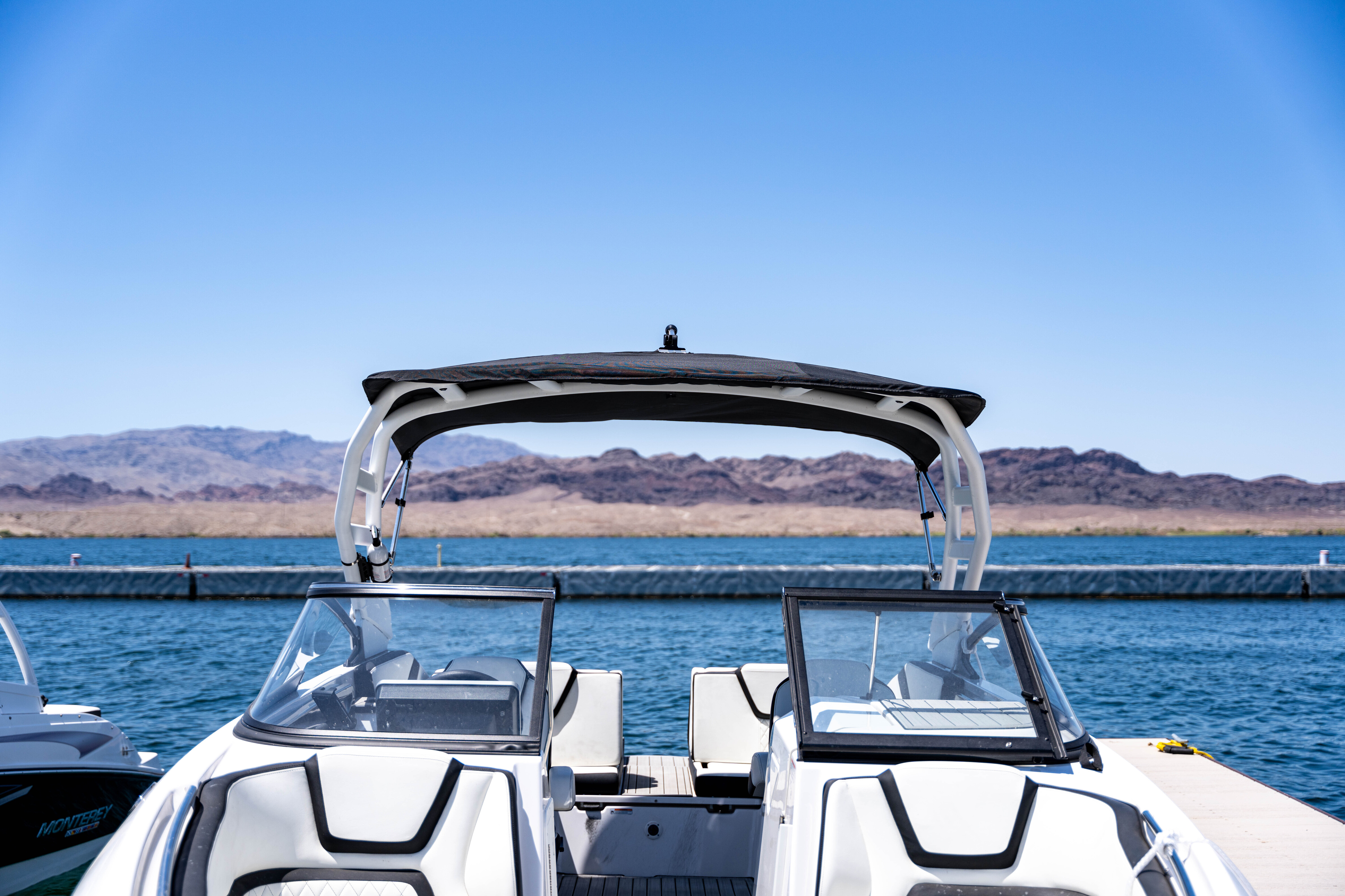 White motorboat docked on blue water with mountains in the background under a clear sky.
