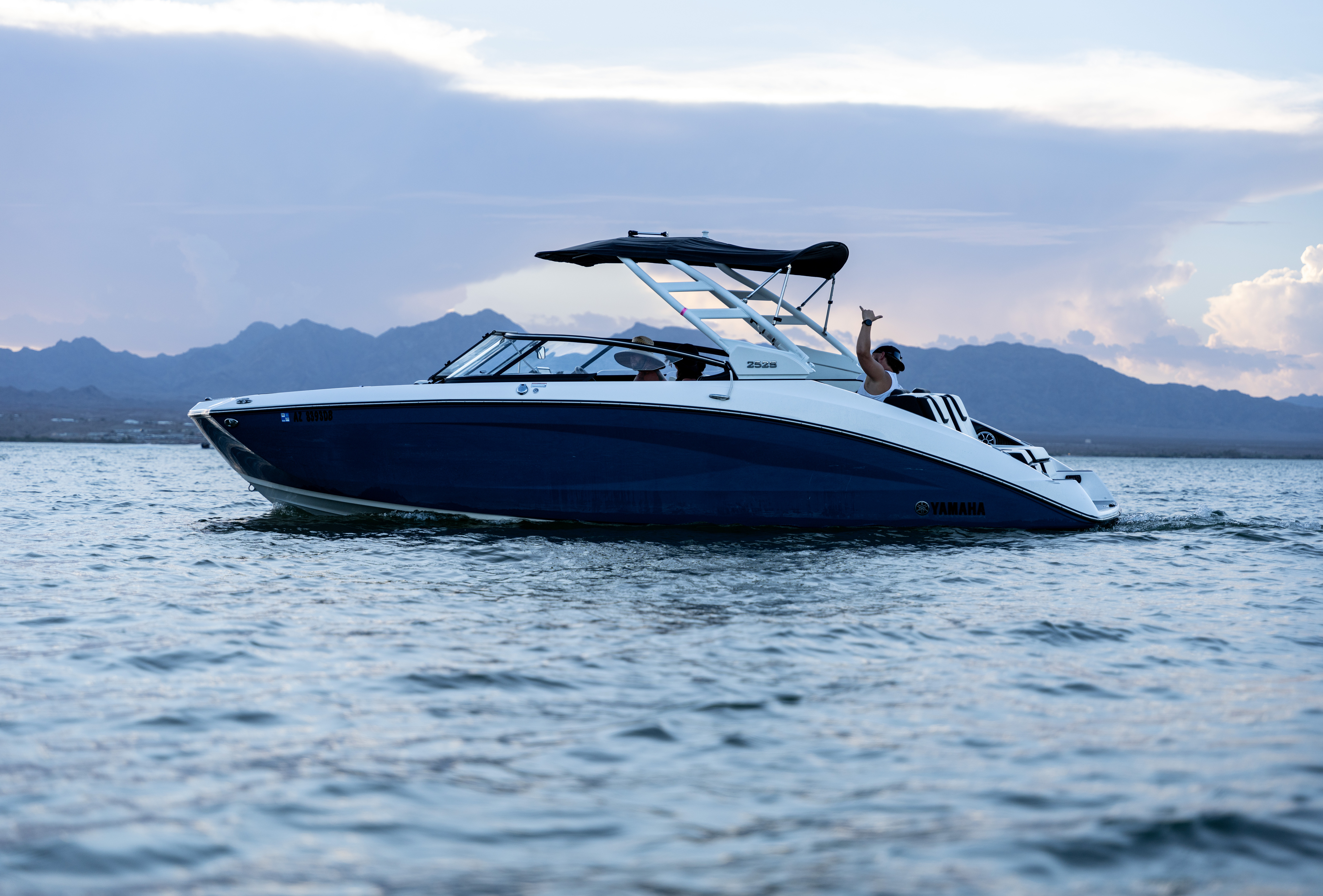Blue and white Yamaha motorboat on calm water with mountains and cloudy sky in the background.